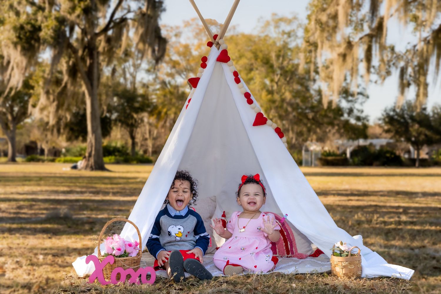 Outdoor family photo session with white teepee tent and heart decorations in a sunlit park.