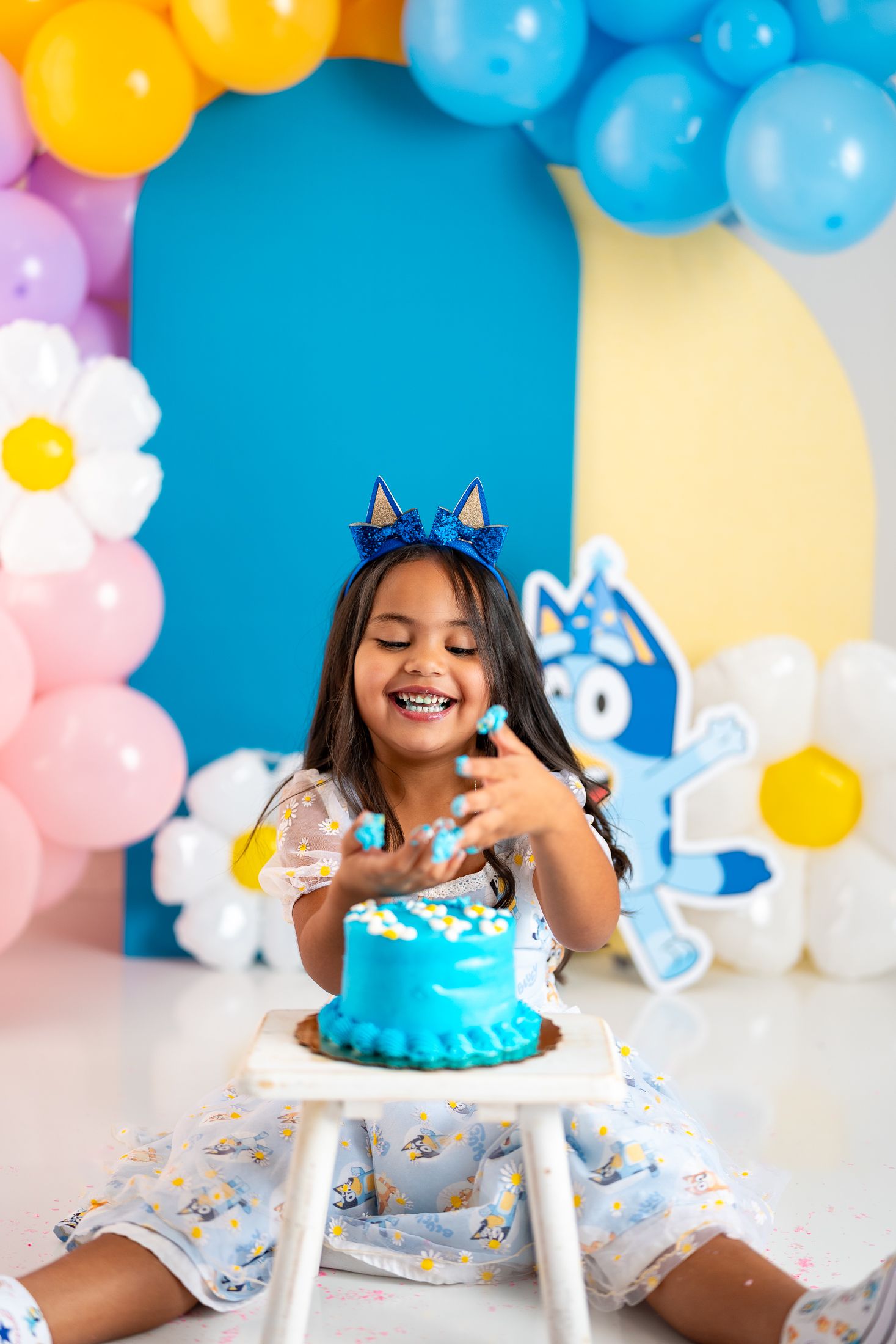 Cake smash photography session with turquoise cake and colorful balloon decorations.