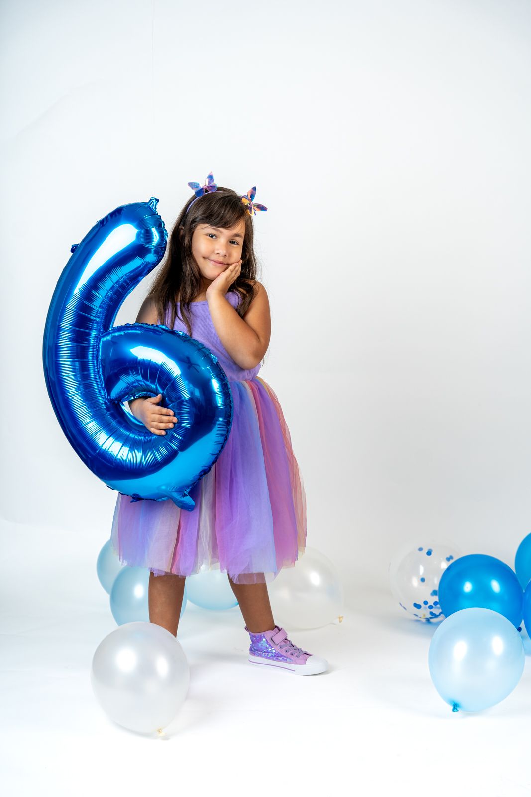 Birthday celebration scene with blue number balloon and purple tulle dress against white backdrop.
