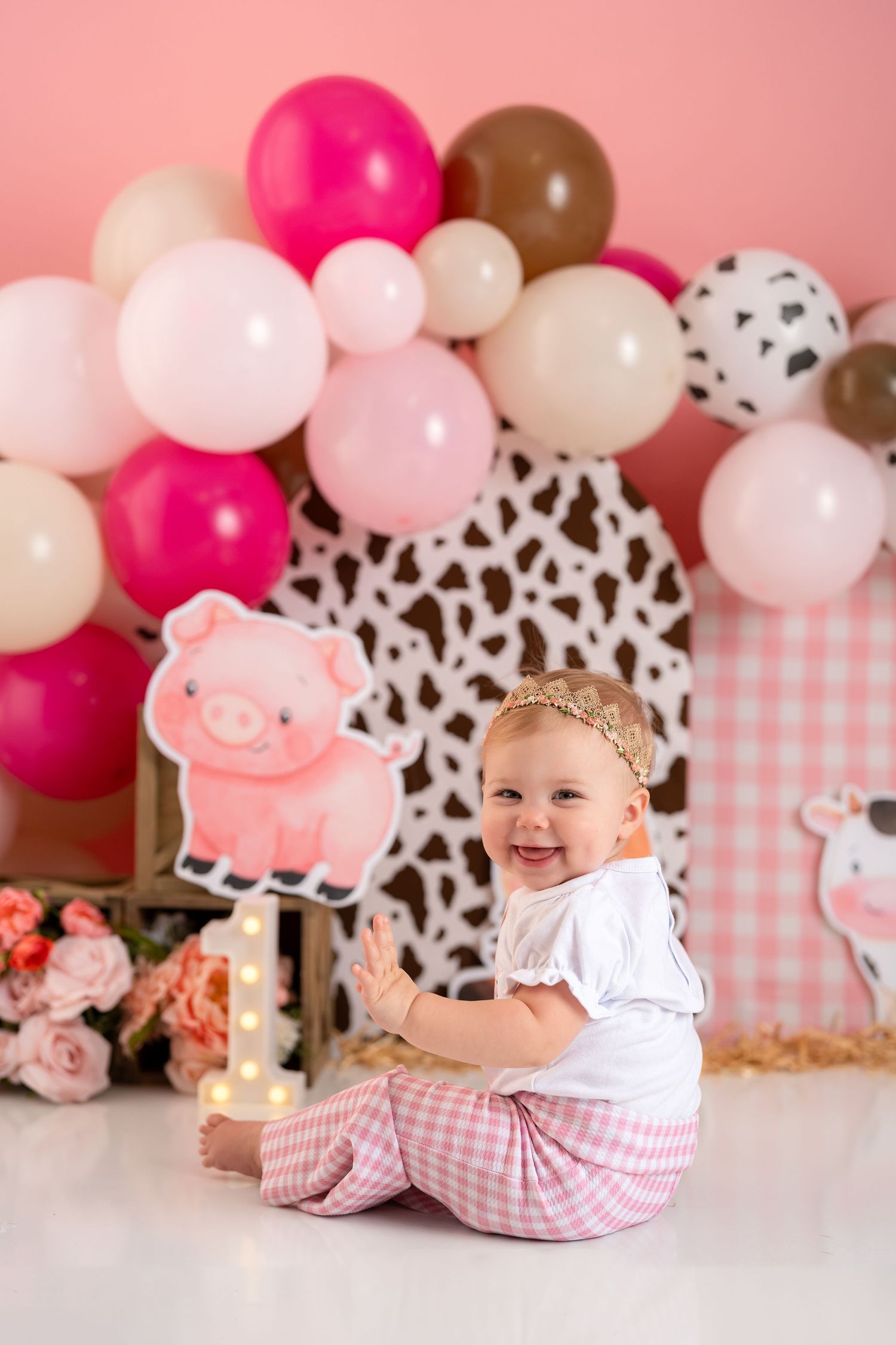 Pink and brown balloon arch with pig theme decorations creates a festive backdrop for a baby photography session.