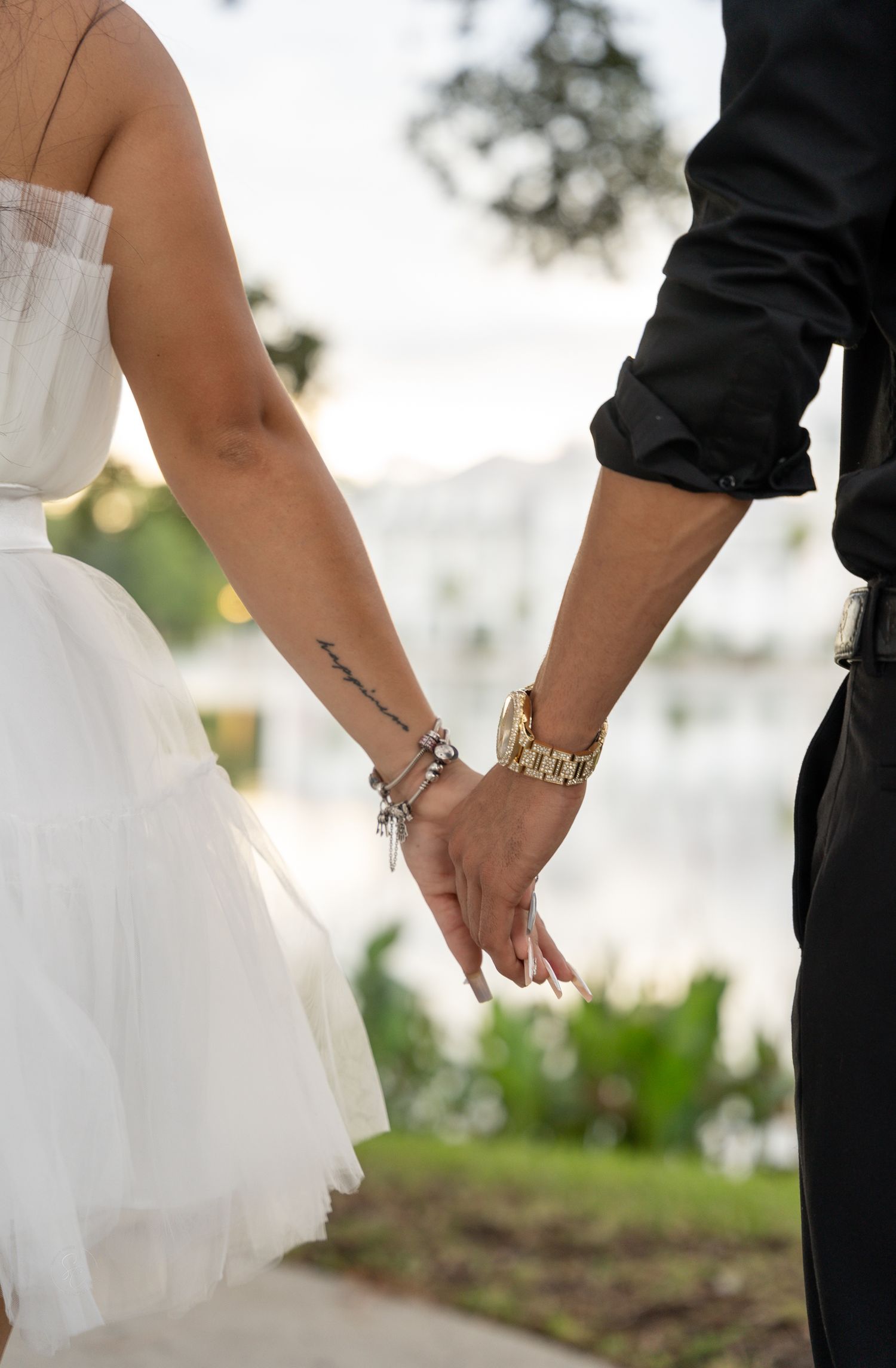 Close-up details of jewelry and hands against white formal dress and black attire.