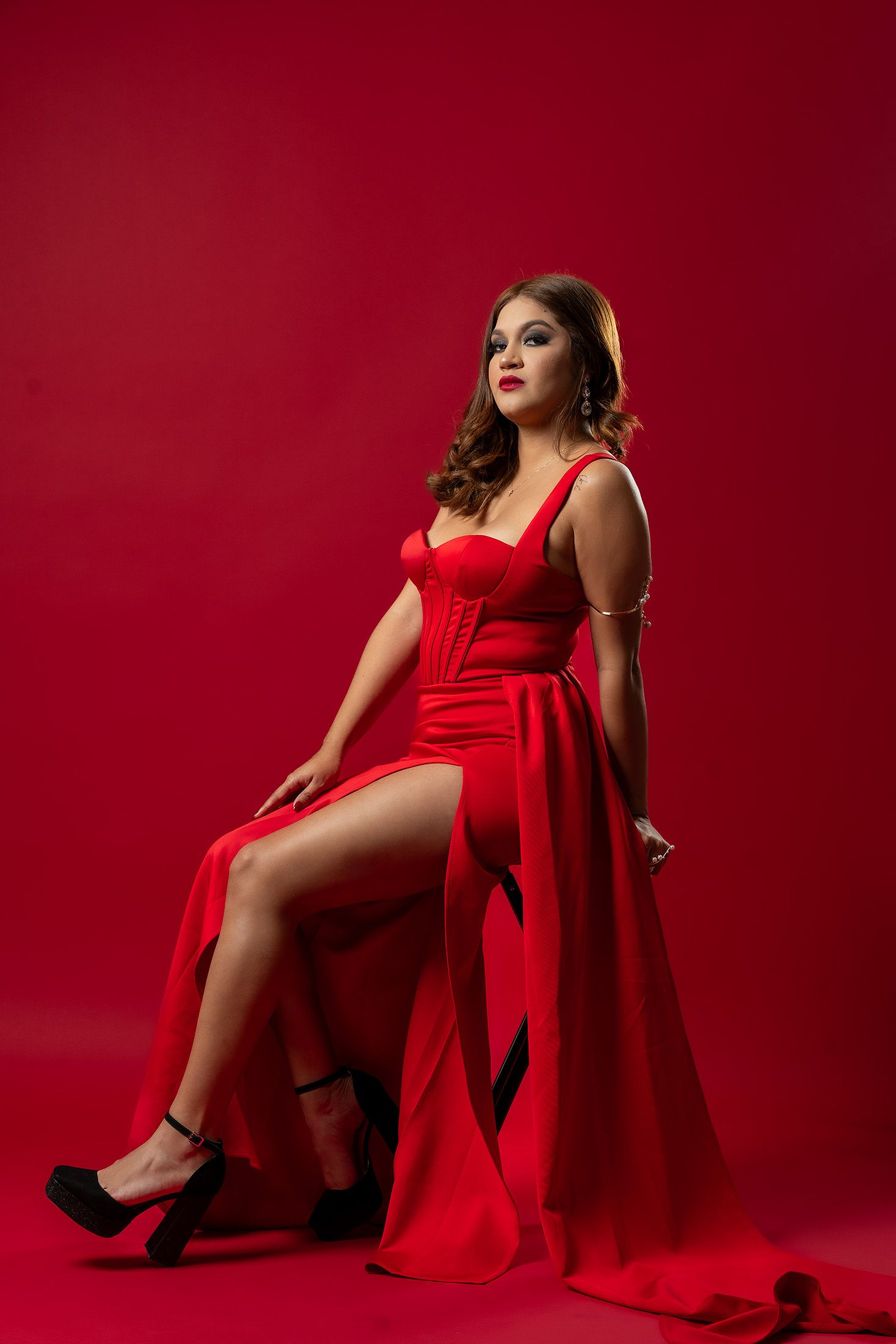 Glamorous portrait session in flowing red dress against crimson background.