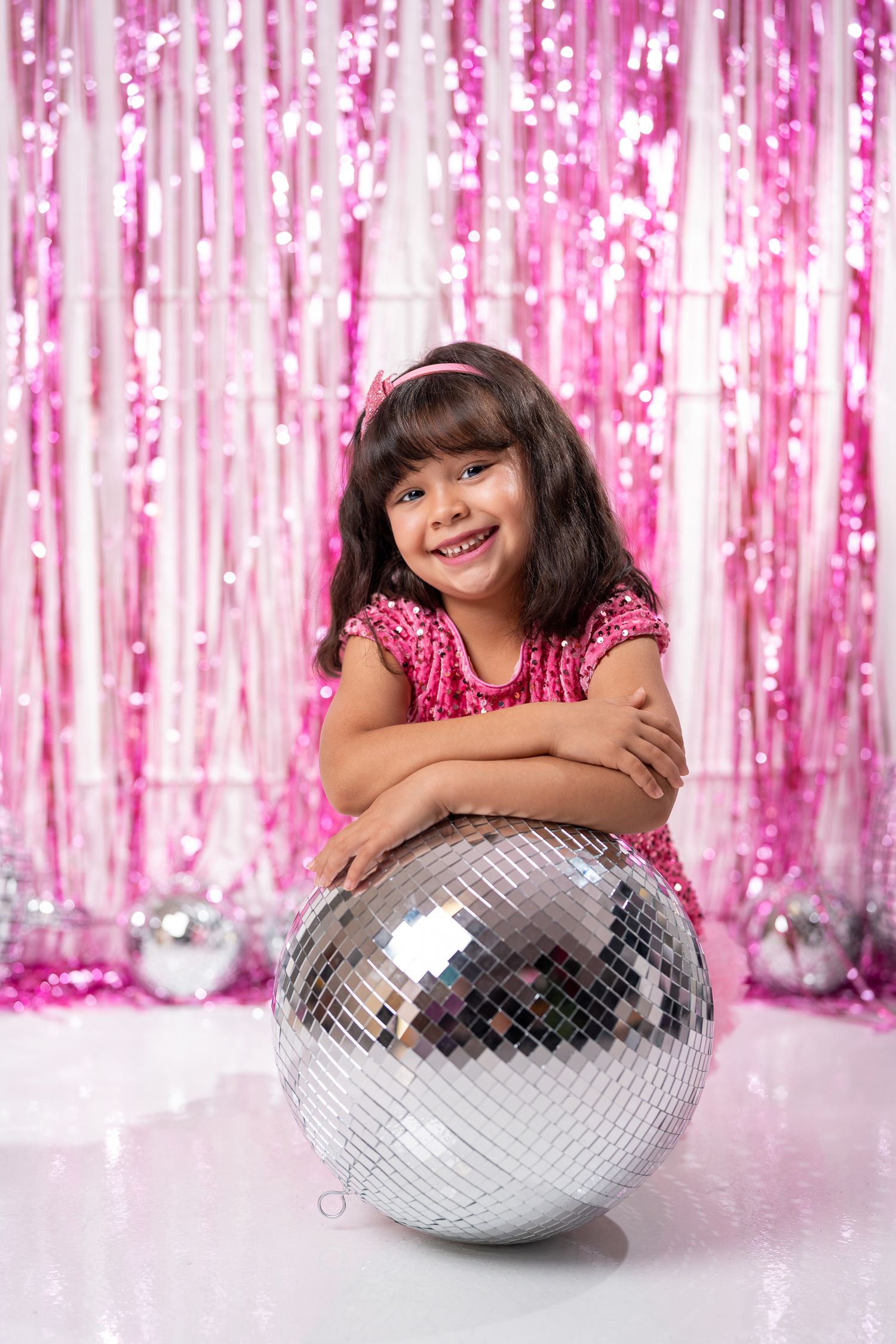 Sparkly pink backdrop frames scene with silver disco ball and festive decorations.