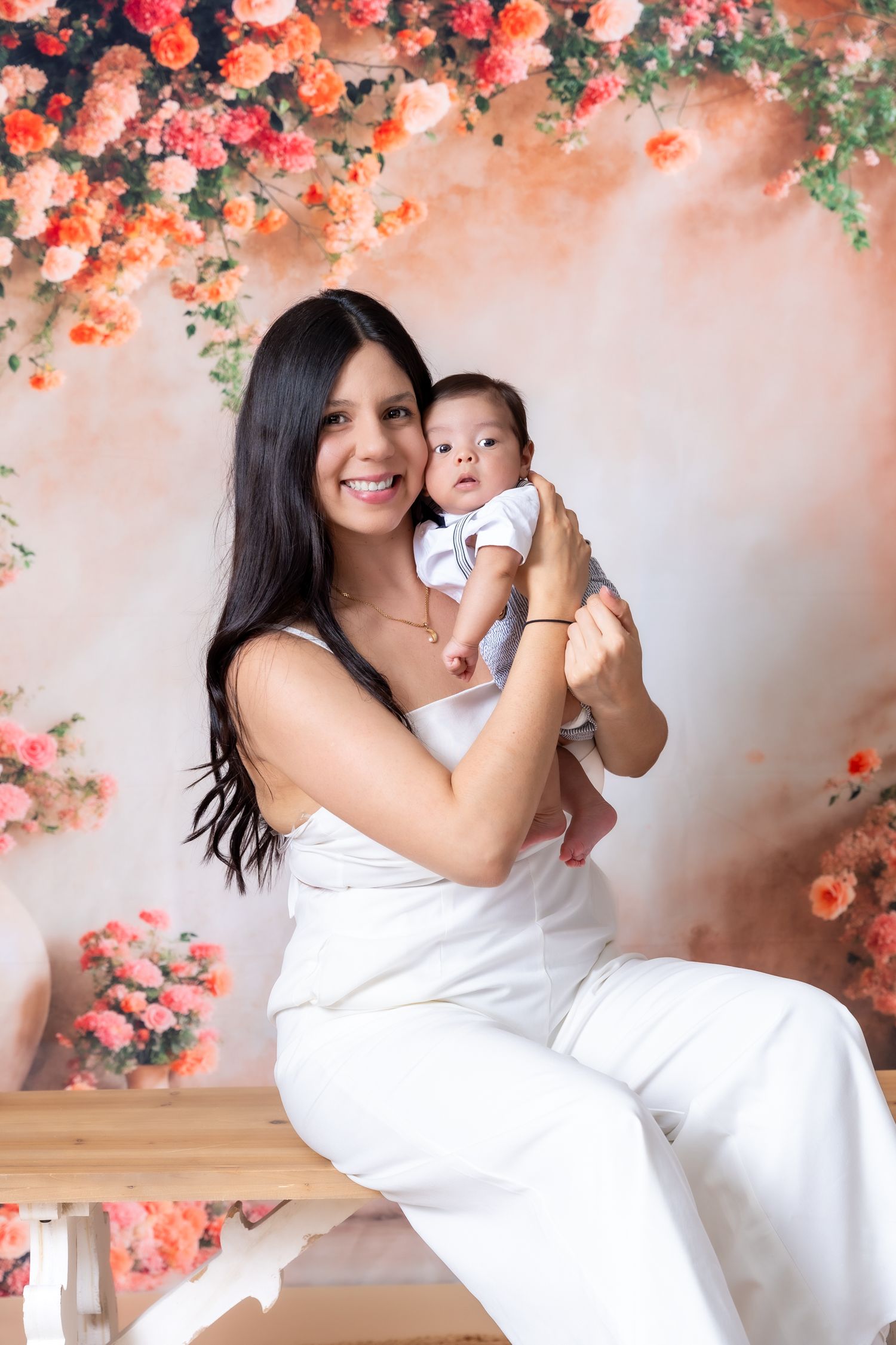 Maternity photoshoot with floral backdrop featuring coral roses and soft lighting.