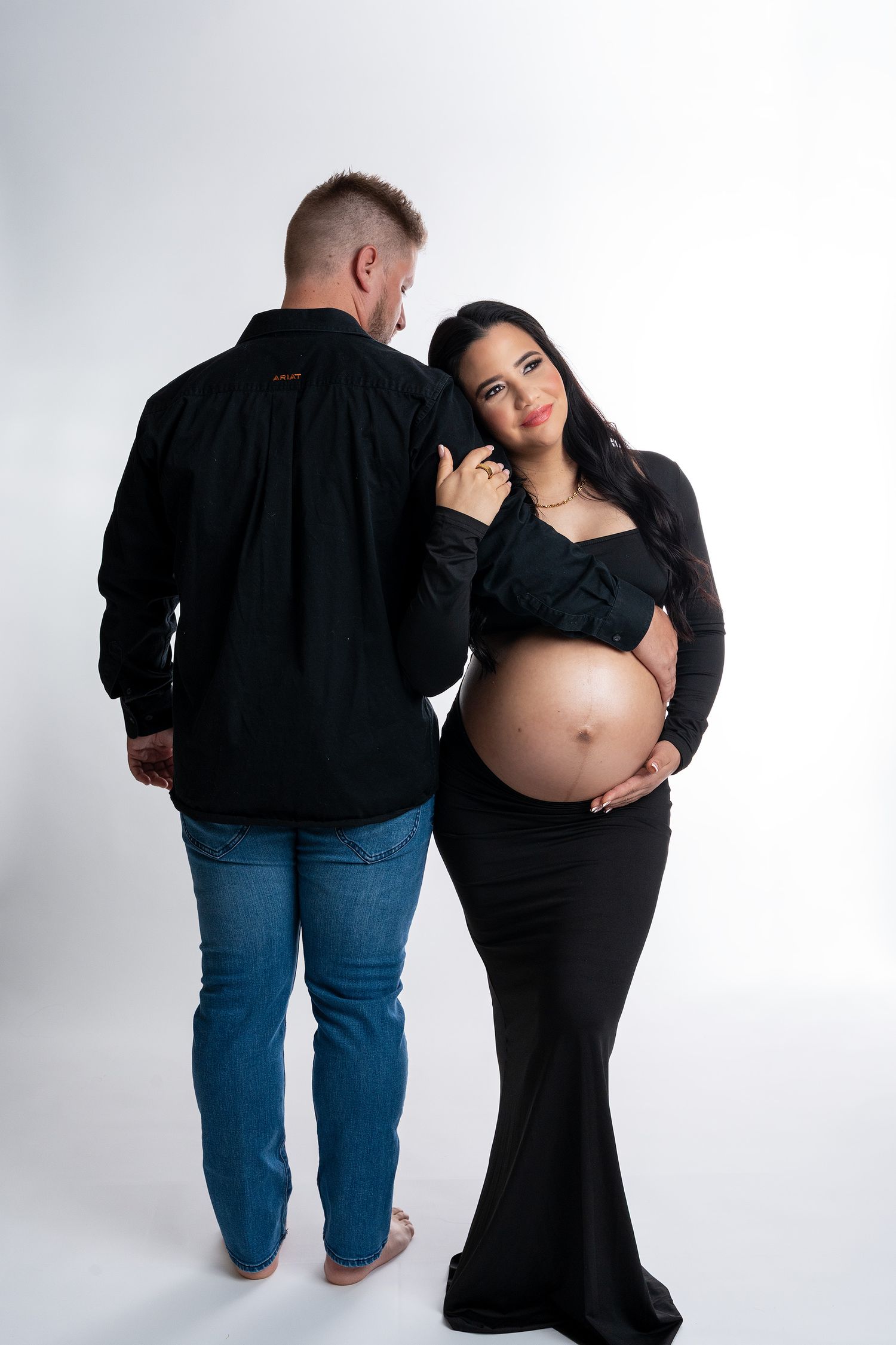 Intimate couple's maternity photos with contrasting black and denim outfits against white backdrop.