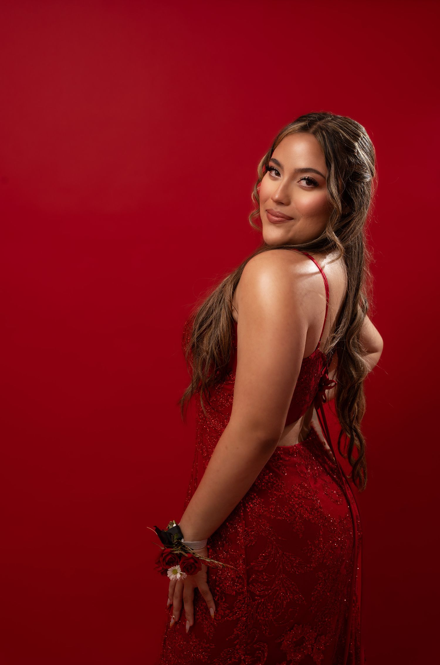 Woman in red dress poses against deep red backdrop in glamorous photoshoot.