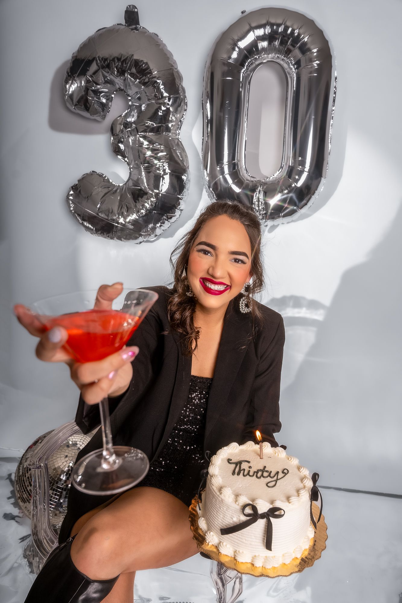 Party scene with silver balloon decorations, red martini glass, and white frosted birthday cake.