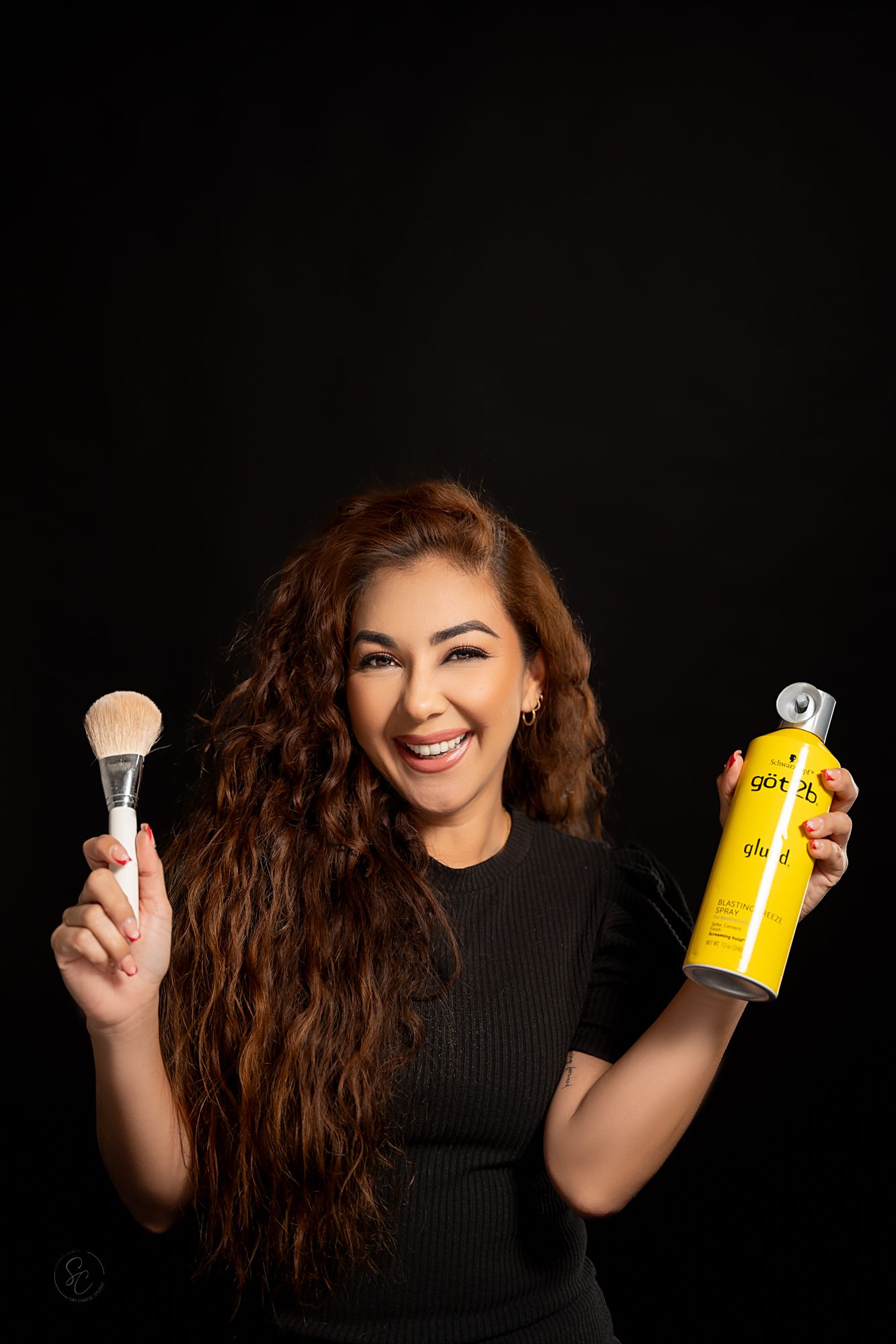 Person shows off hair care products while posing expressively against dark studio backdrop.