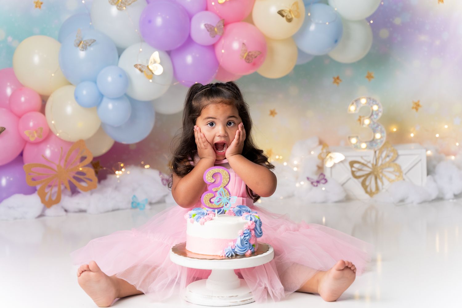 Festive cake smash setup with pastel balloon arch and pink decorations.