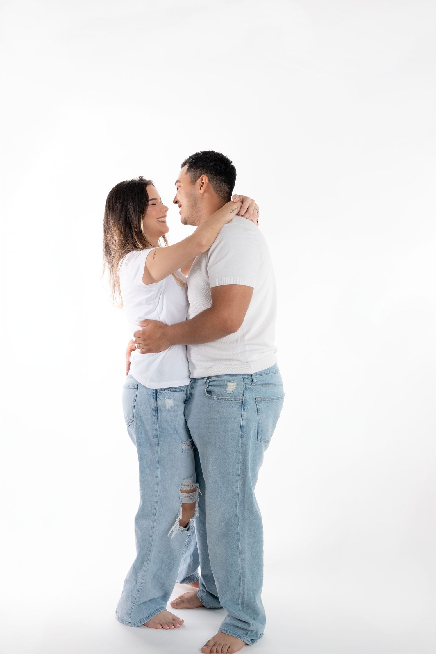 Minimalist couple photoshoot with matching white tops and distressed jeans against white background.