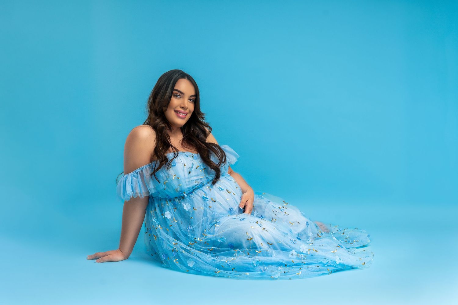 A figure in a flowing light blue dress poses elegantly against a bright turquoise backdrop.