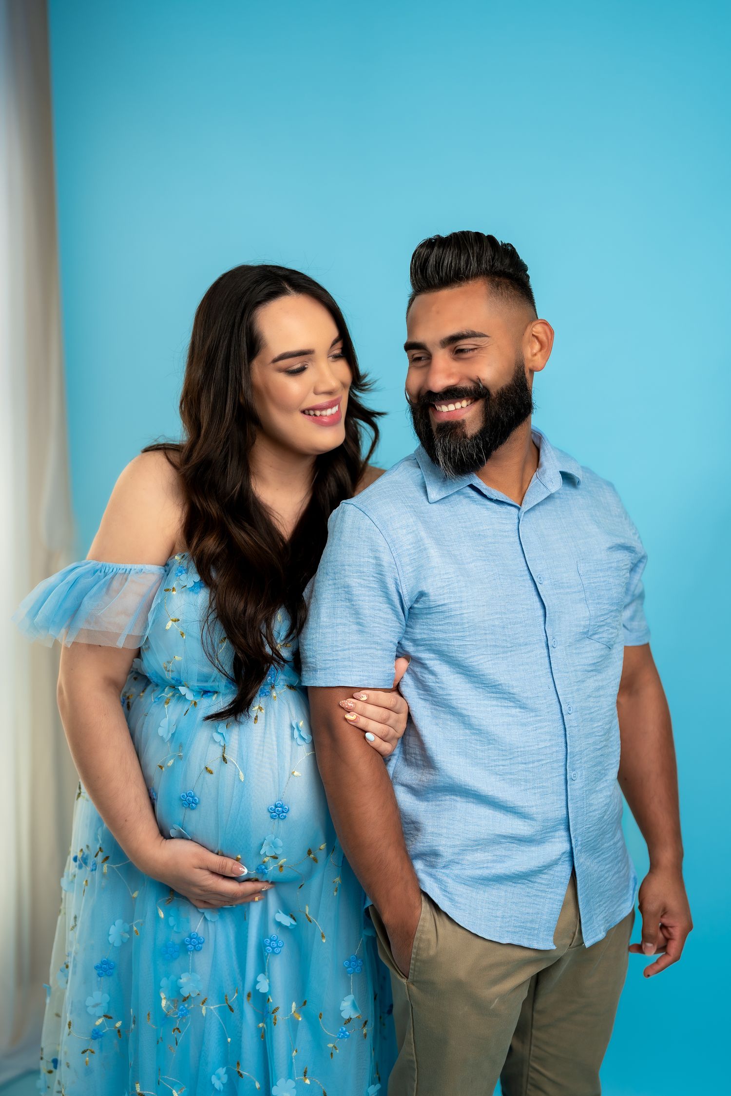 Playful couple shares intimate moments in blue outfits against bright turquoise background.
