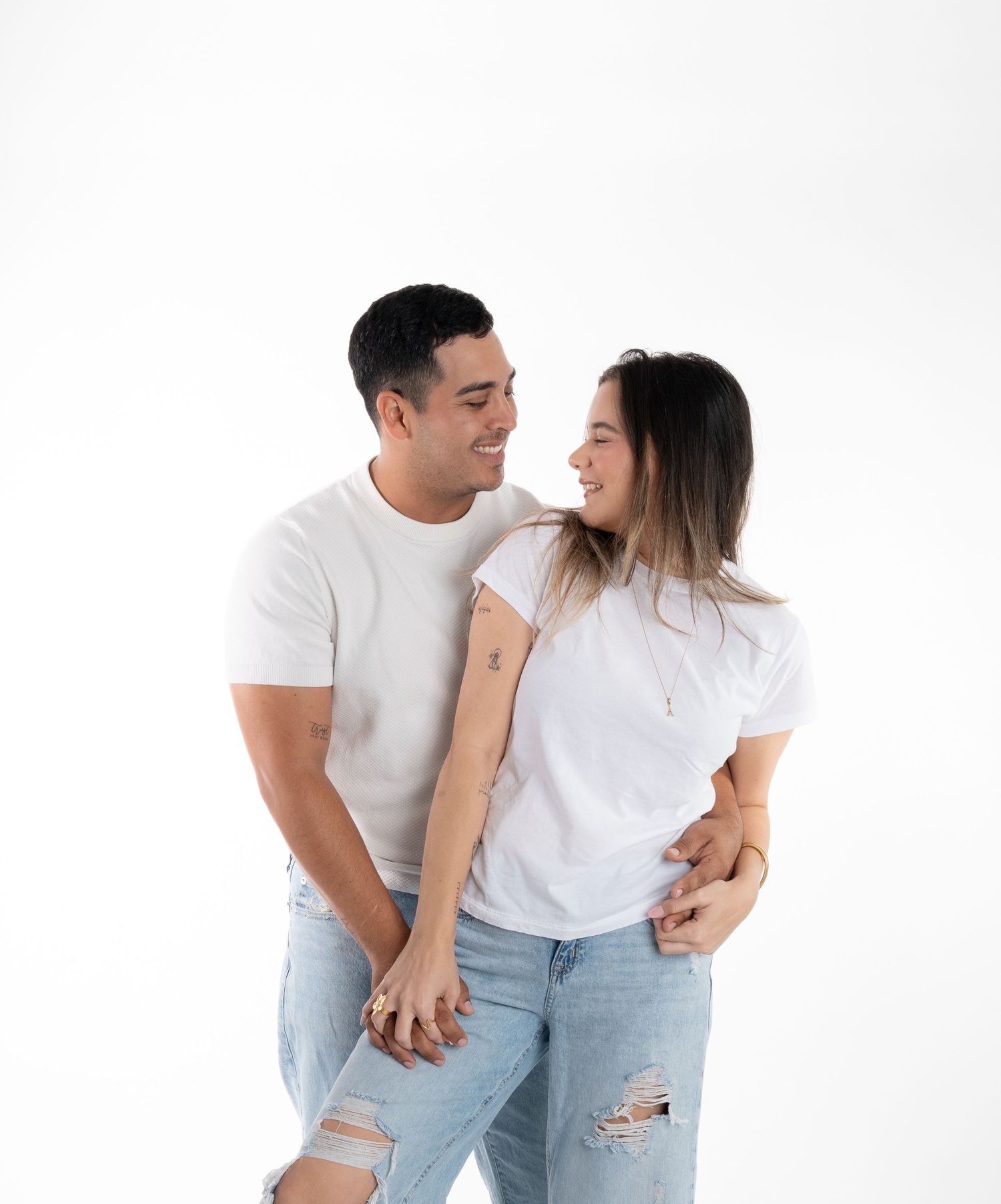 A couple in white t-shirts and ripped jeans share an intimate moment against a white backdrop.