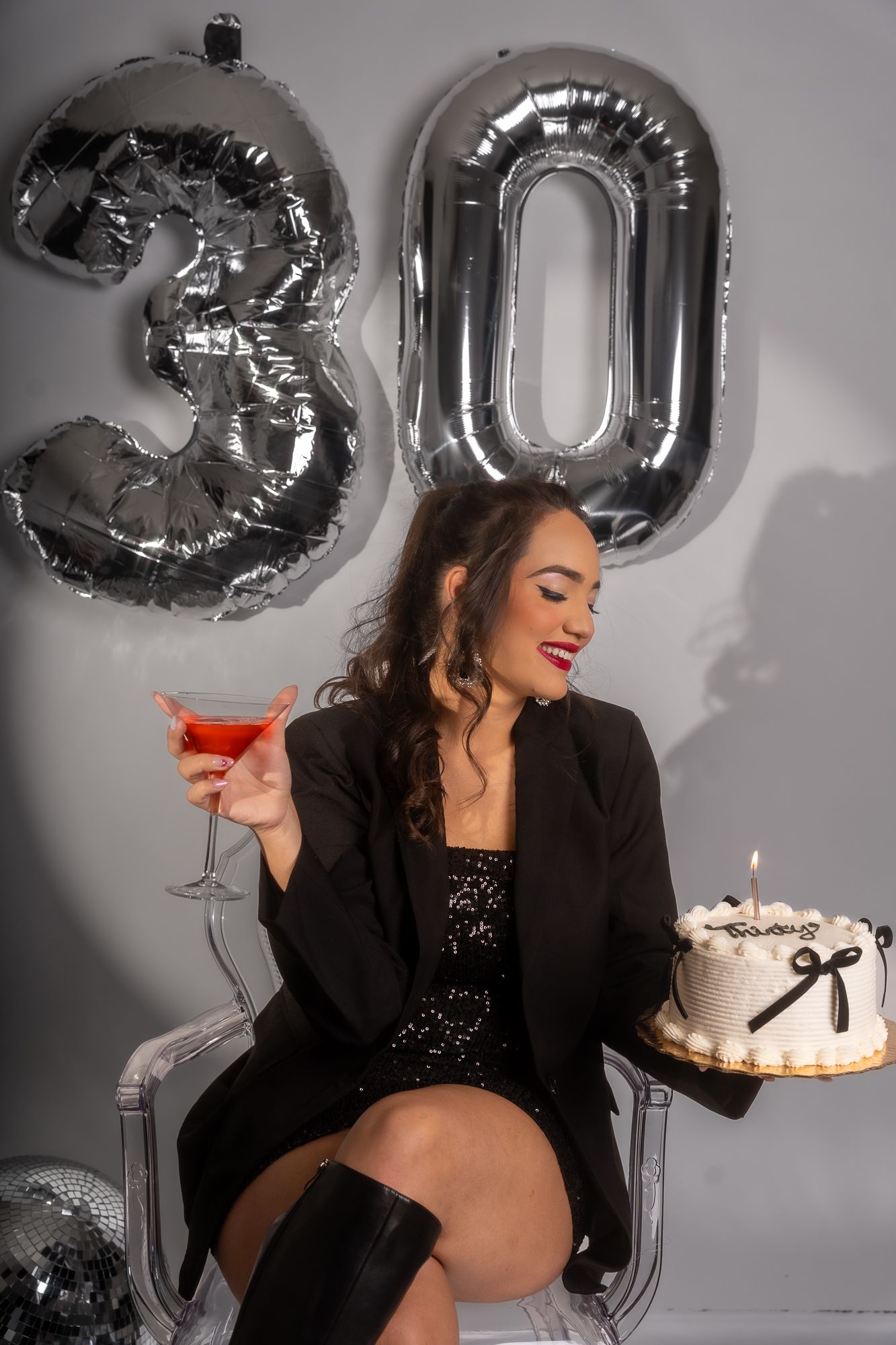 Elegant birthday scene with silver '30' balloons, cocktail glass and white cake with black bow decoration.