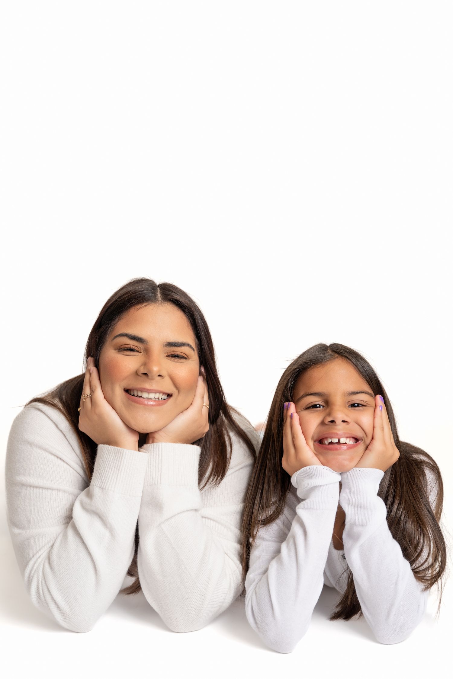 Two people in white sweaters lying down and smiling while resting their faces on their hands.
