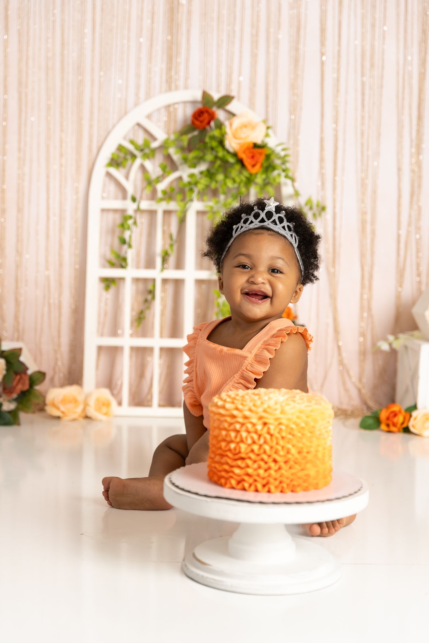 Peach ombre ruffle cake against floral backdrop for first birthday celebration.