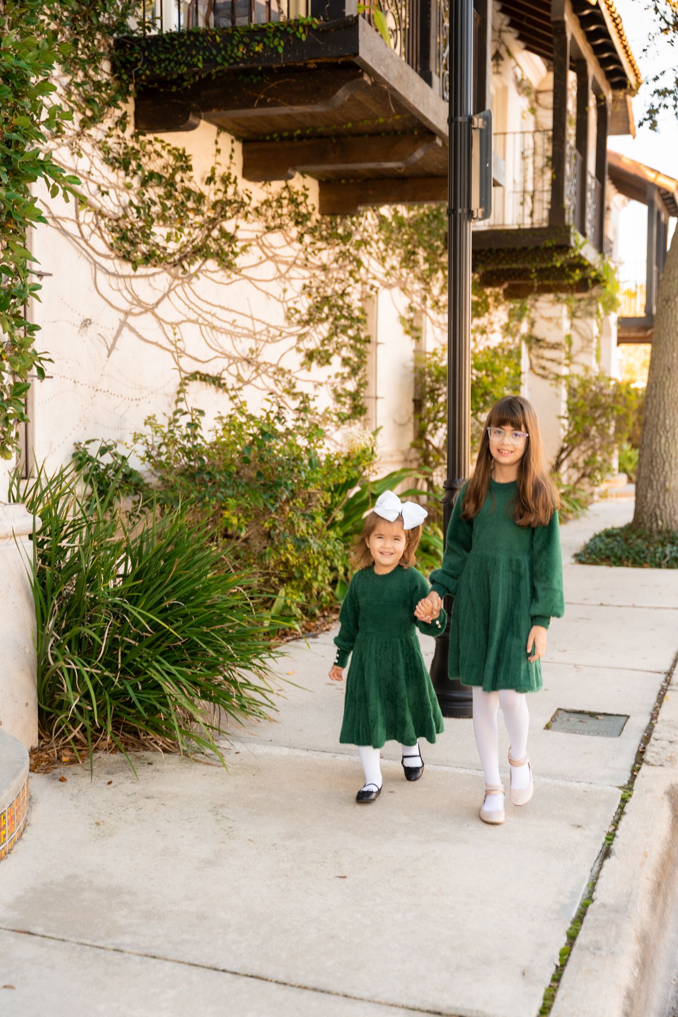 Family wearing coordinated green outfits poses along architectural walkway with vines.