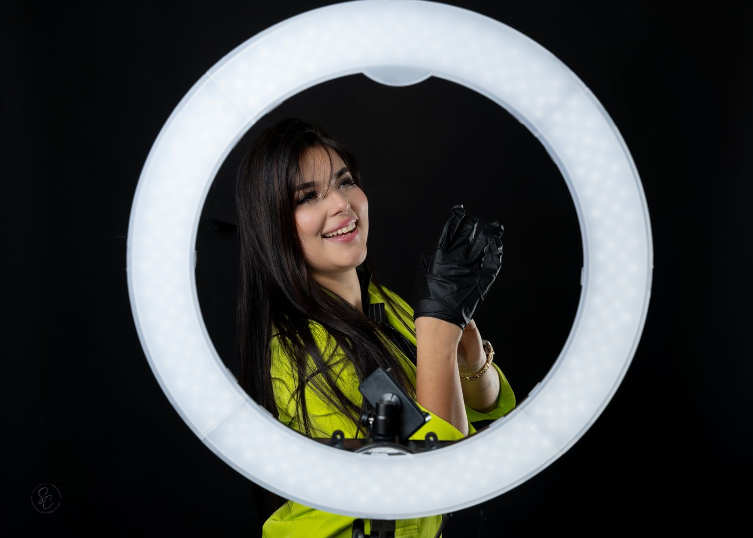 Professional portrait through a ring light showing a person in yellow safety vest and black gloves against dark background.