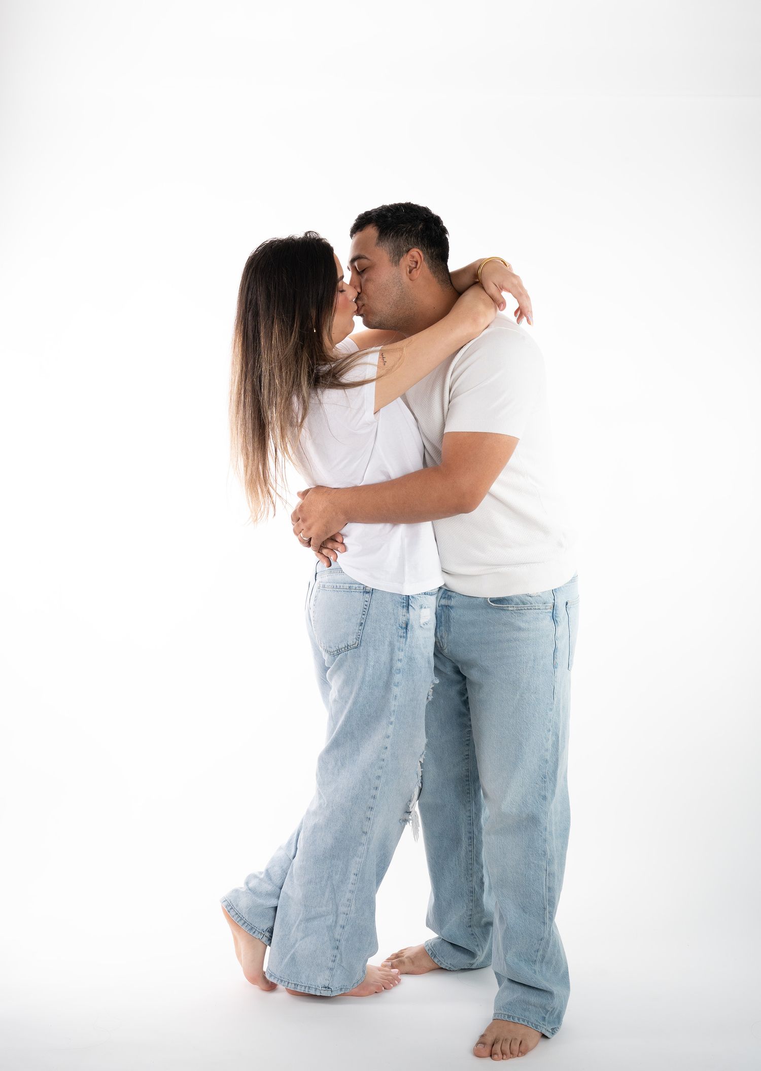 A tender moment between a couple in white t-shirts and jeans against a minimalist white background.