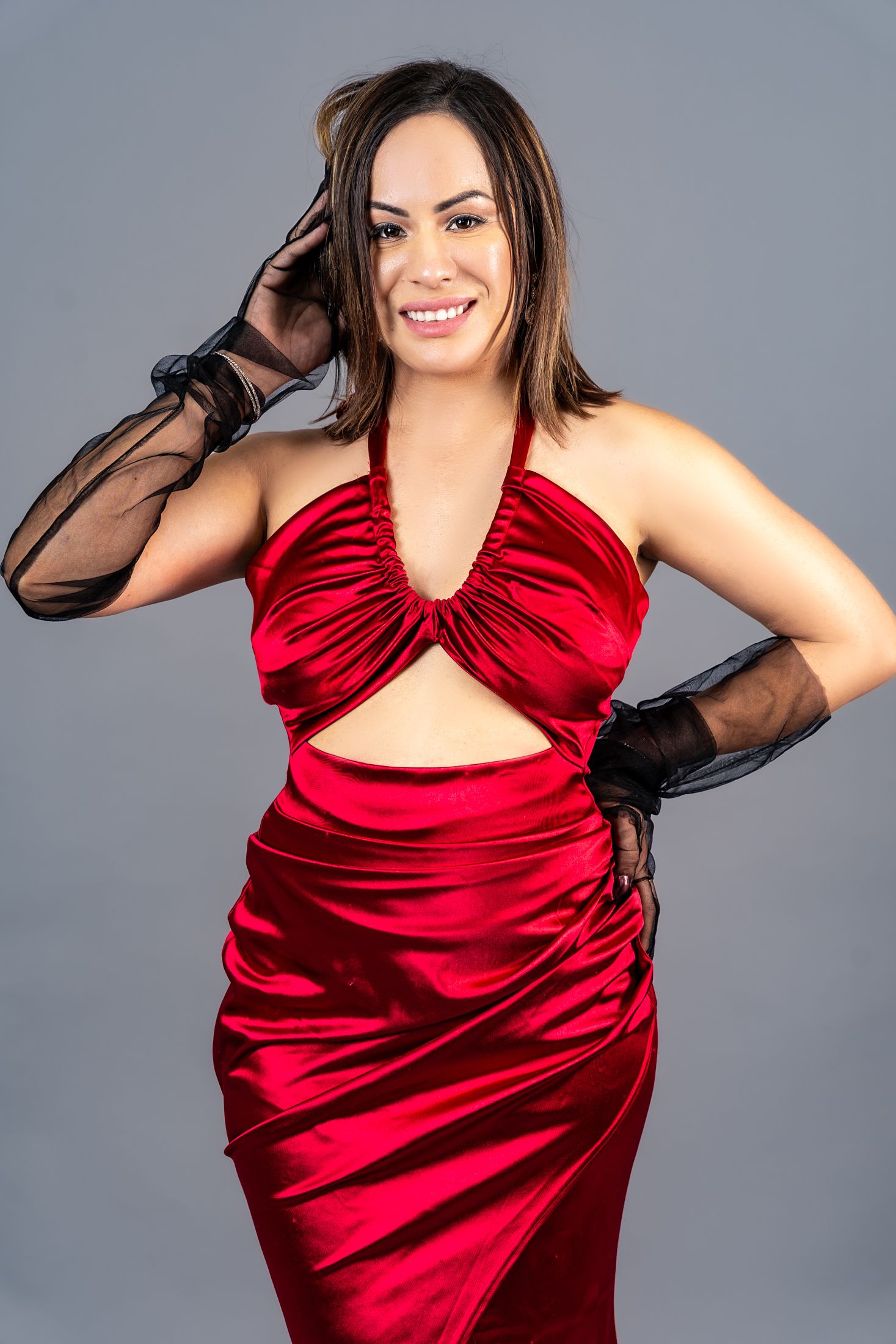 Woman in red satin dress and black gloves poses elegantly against gray background.