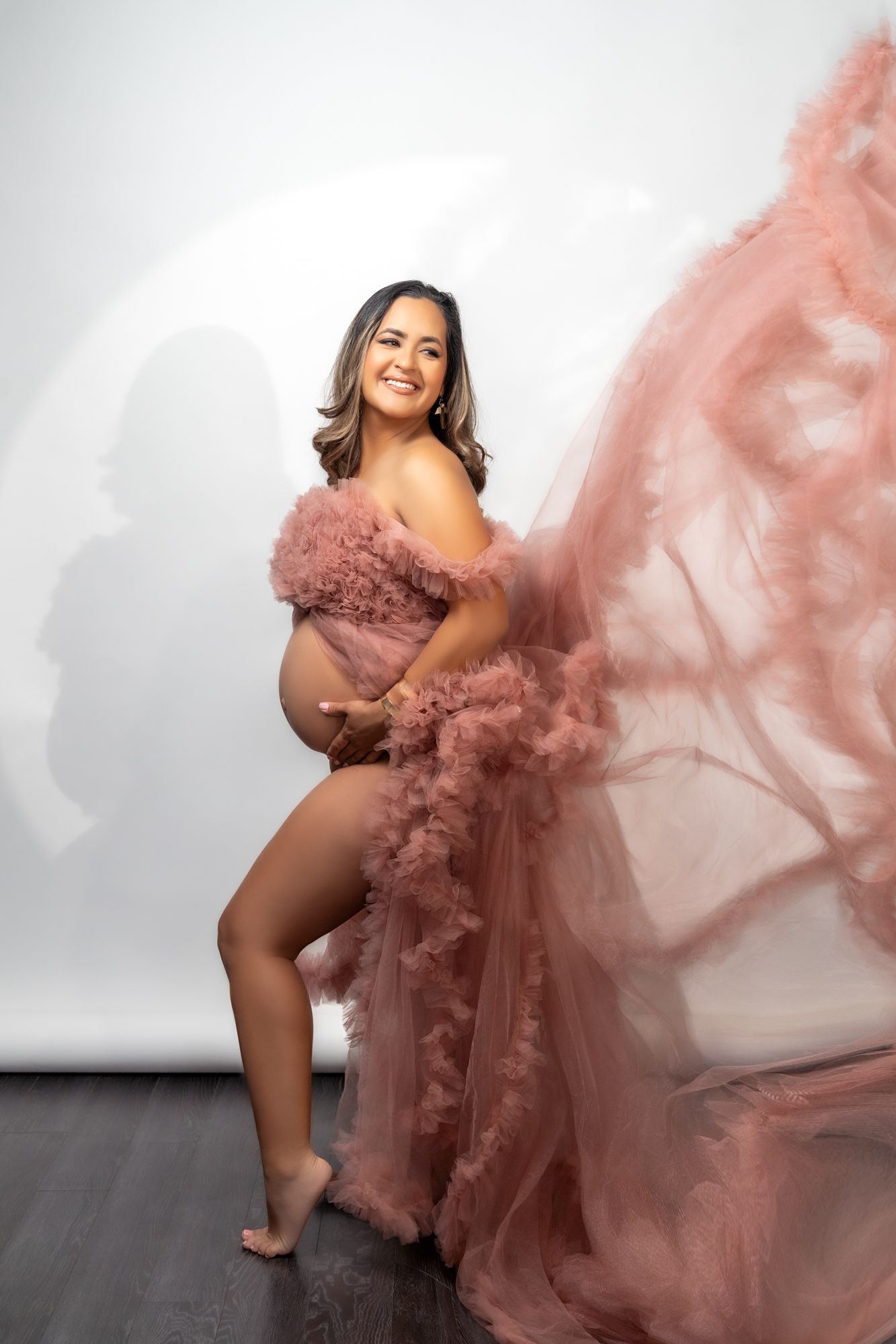 Dynamic maternity photoshoot featuring flowing dusty rose tulle gown with dramatic movement.