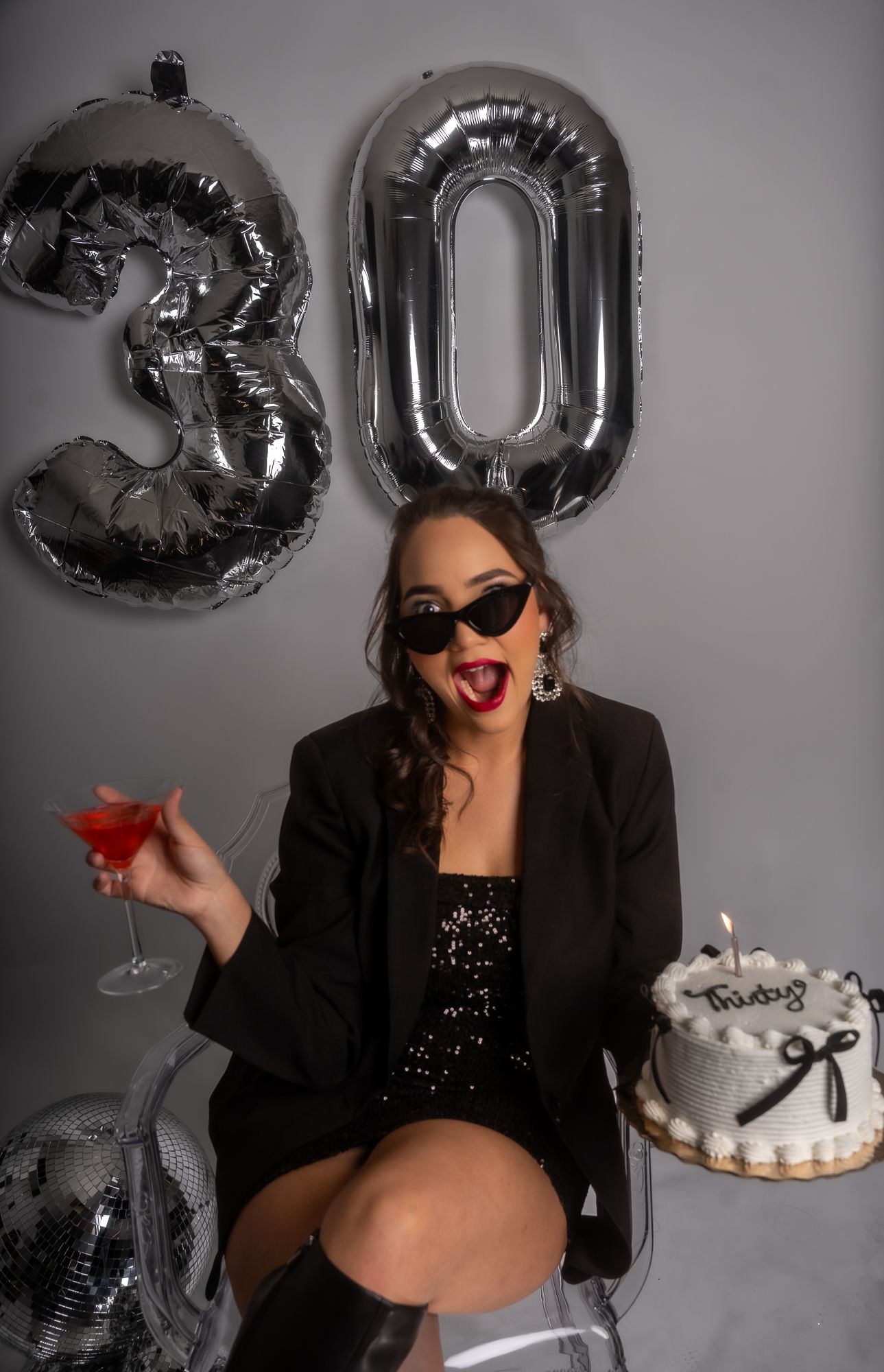 Festive 30th birthday setup with silver balloons, sunglasses, cocktail and decorated white cake.
