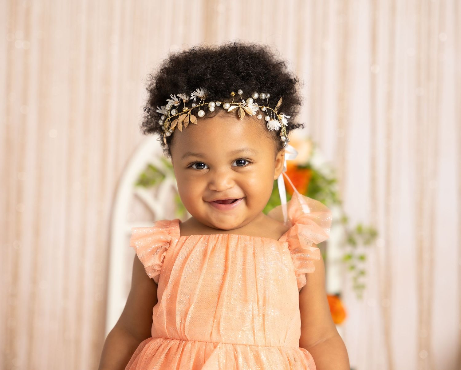 Peach dress celebration portrait with floral backdrop and natural lighting.
