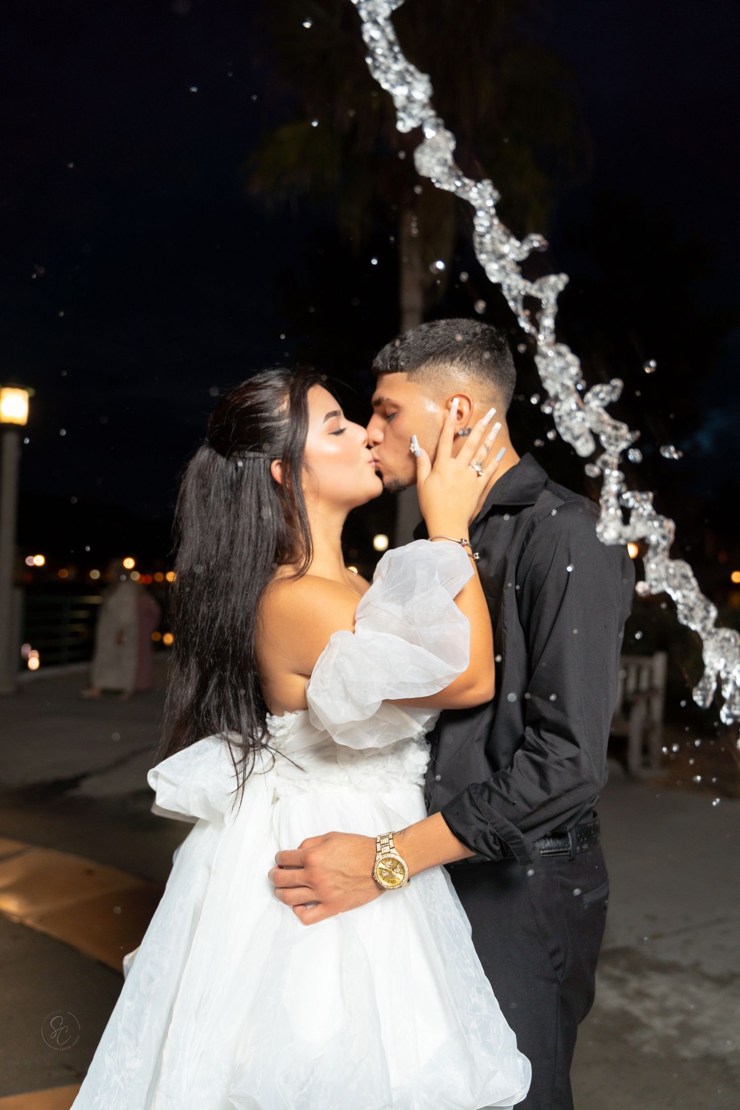 A romantic kiss under illuminated water fountains at night.