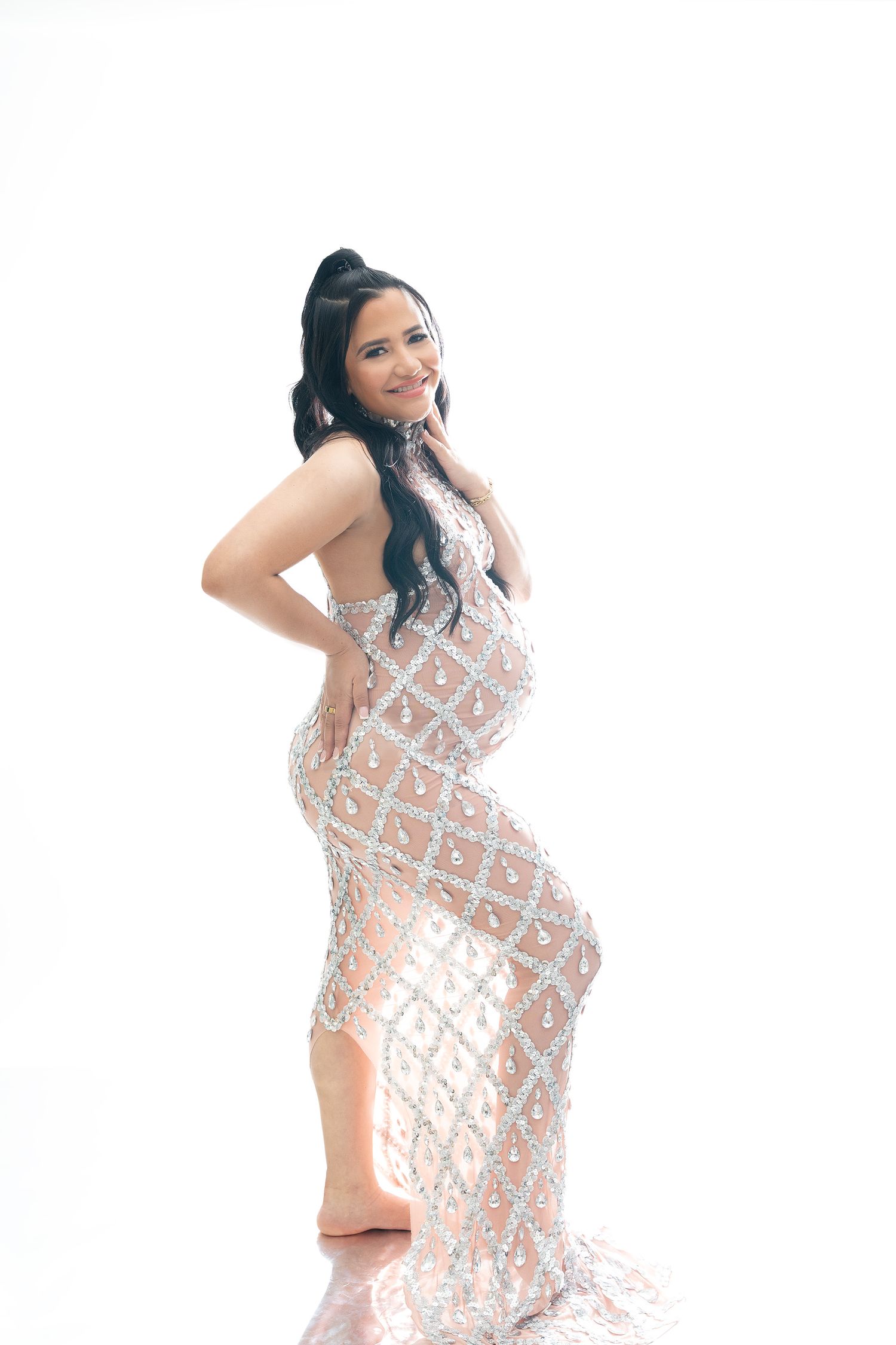 Glamorous maternity photoshoot featuring a sparkly silver sequined gown against a light background.