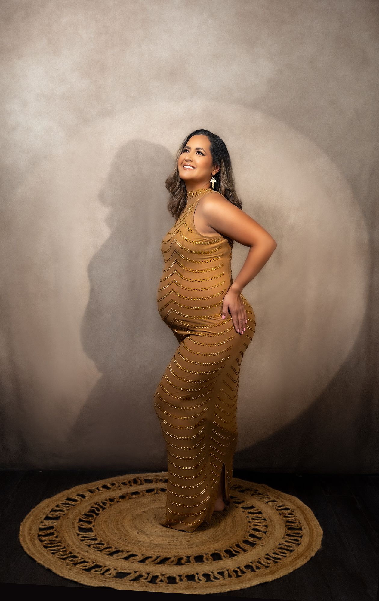 Artistic maternity portraits with ruched caramel dress against textured beige background.