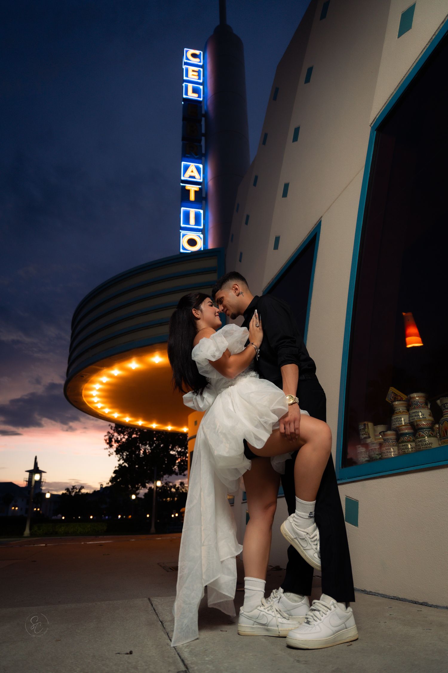 Urban nighttime couple photoshoot with dramatic lighting against illuminated building facade.