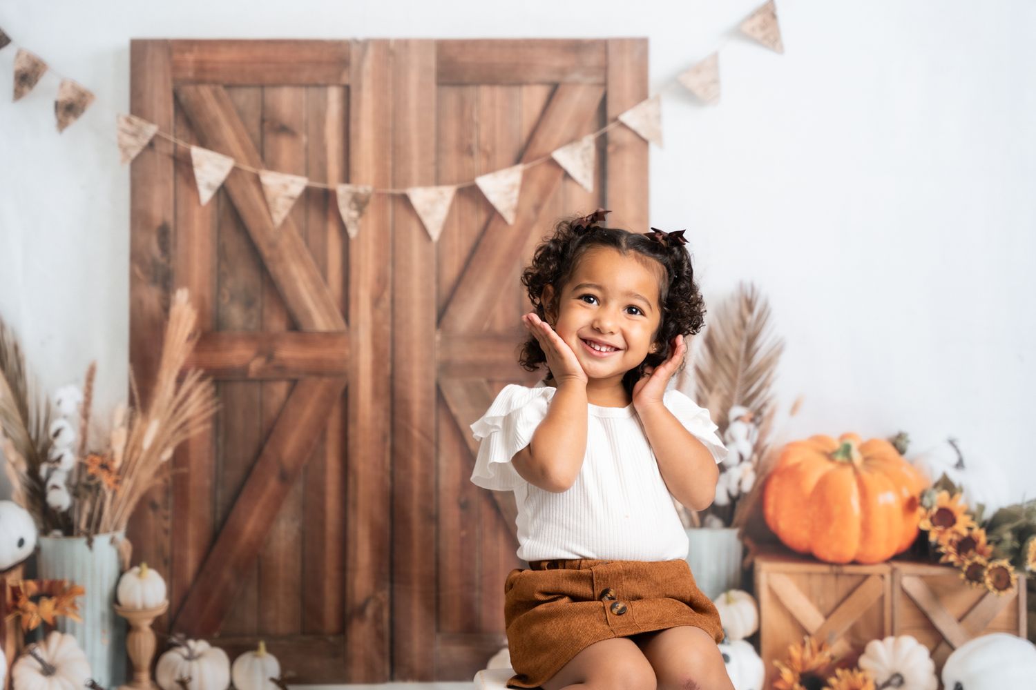 Rustic fall photo session setup with wooden barn backdrop, pumpkins, and orange bunting decorations.