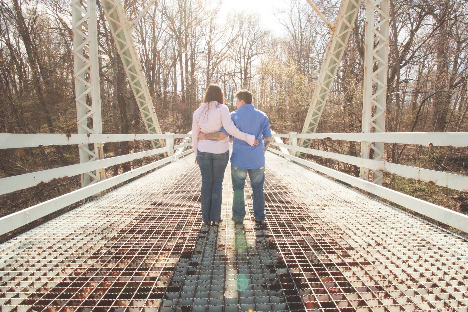 Couple walking together on a wooden bridge surrounded by bare winter trees.