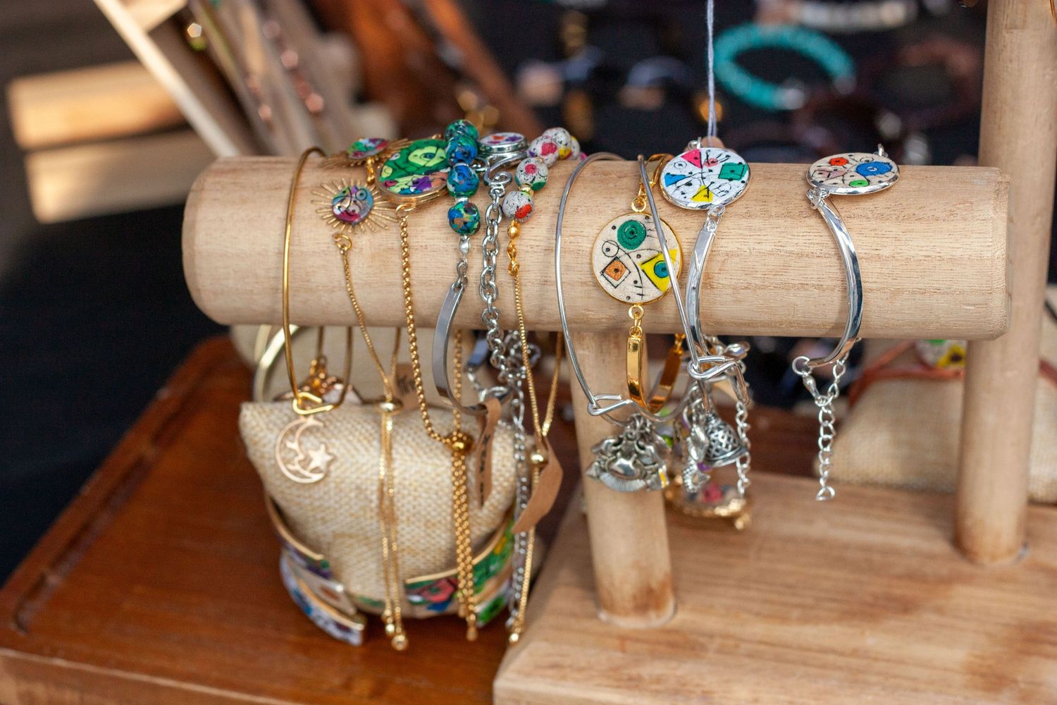 Colorful gemstone bracelets displayed on a wooden jewelry stand, featuring gold and silver chains with floral designs.