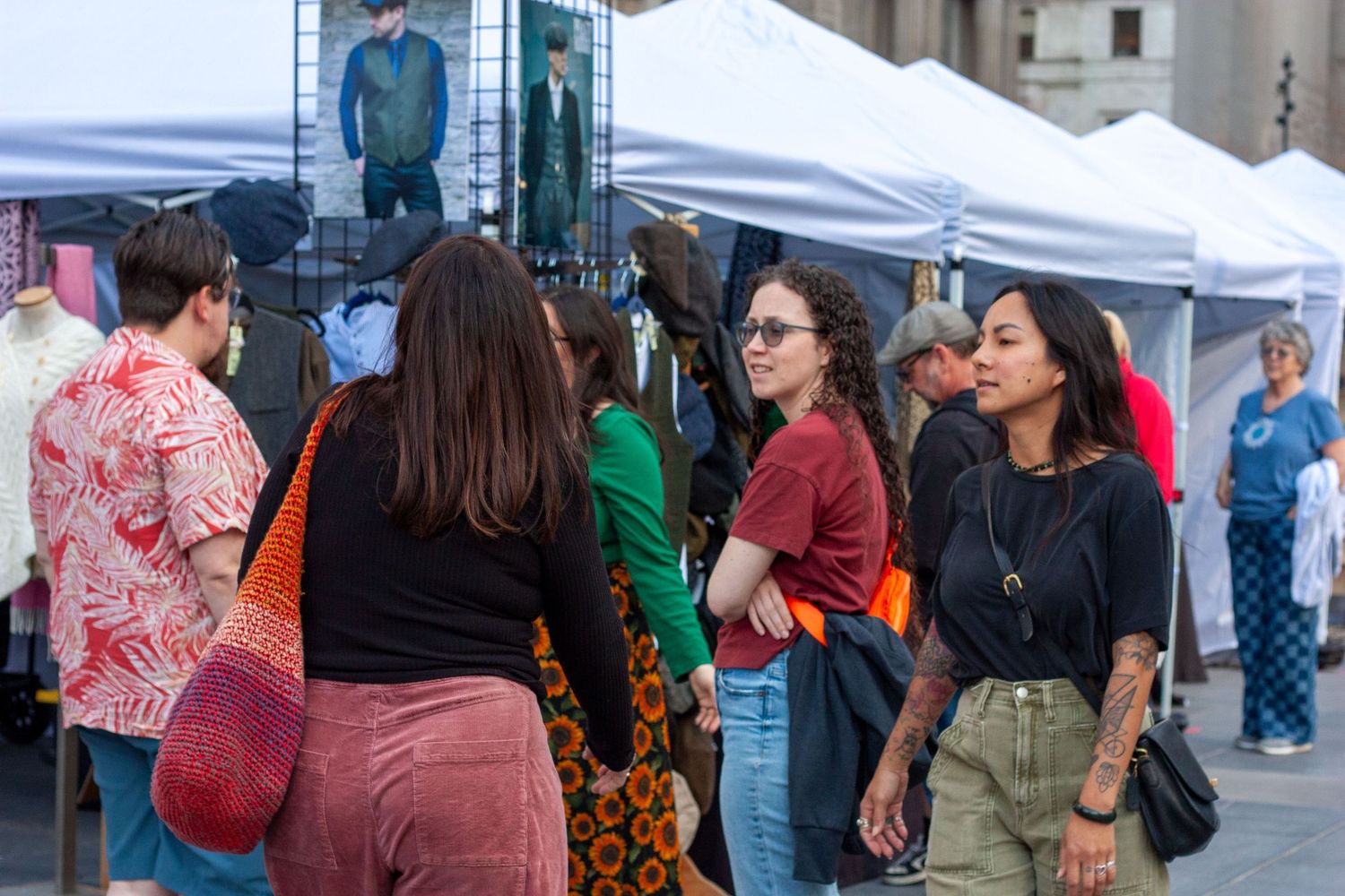People browsing an outdoor market with white tents, shopping for clothing on a sunny day.