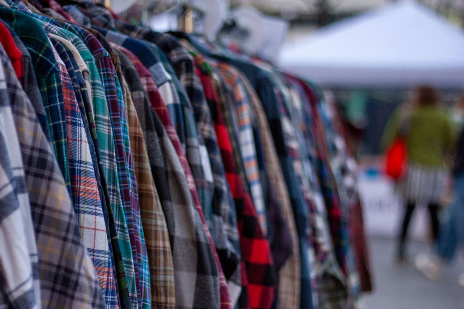 Colorful plaid flannel shirts hanging on a rack at an outdoor market or flea sale.
