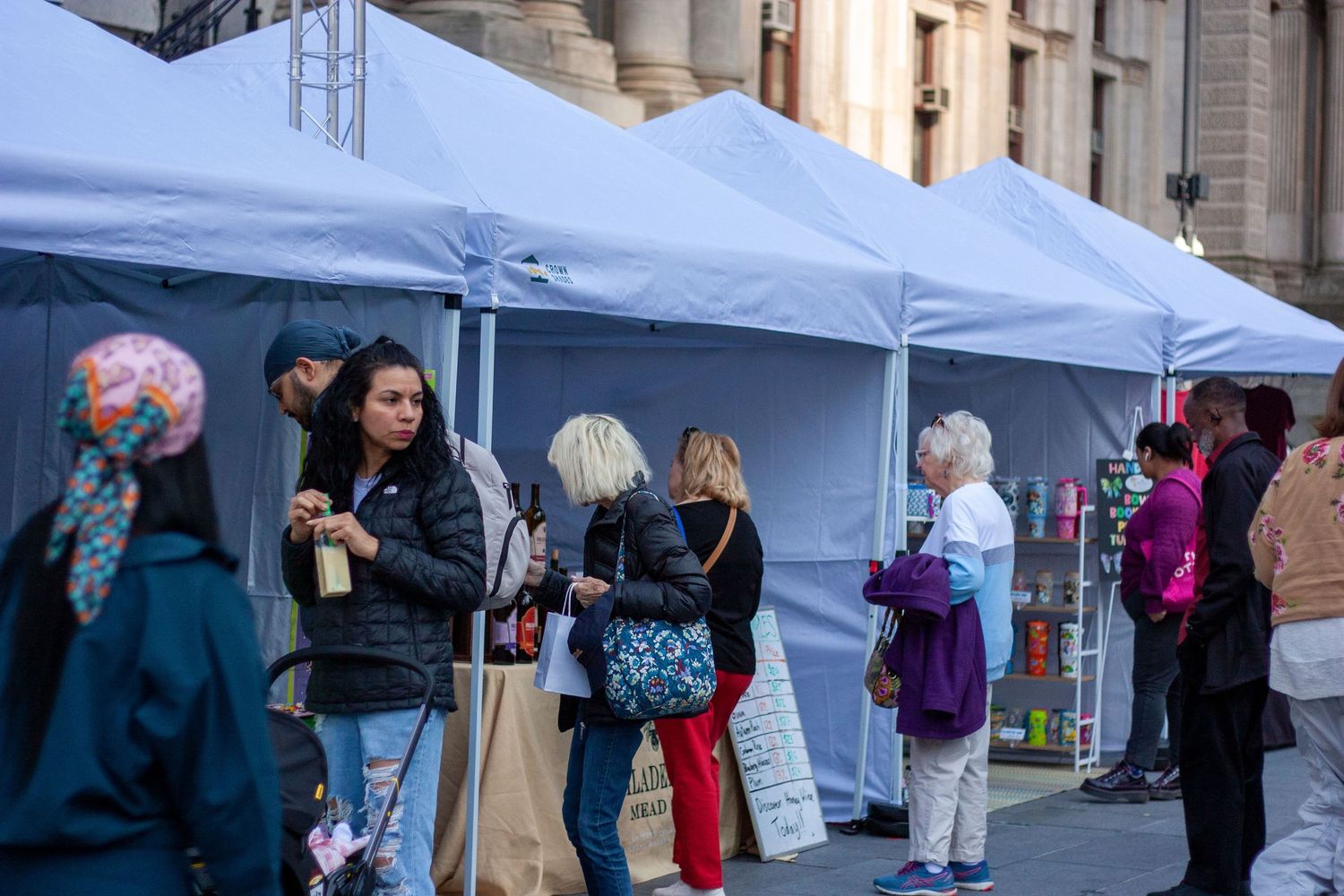 People browsing outdoor market stalls under white canopy tents at a busy street festival.