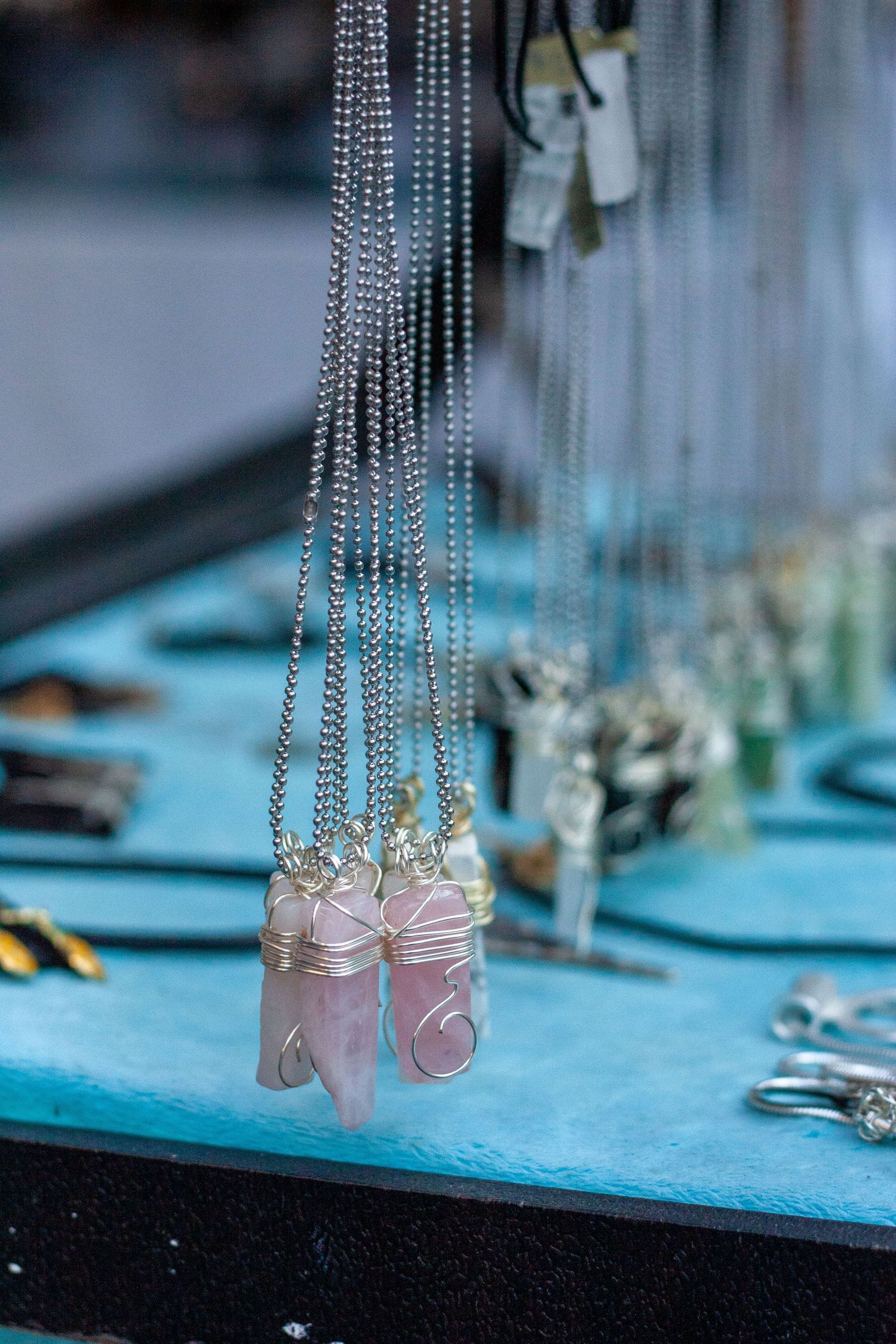 Pink rose quartz crystal pendant necklaces wrapped in silver wire displayed on a turquoise jewelry stand.