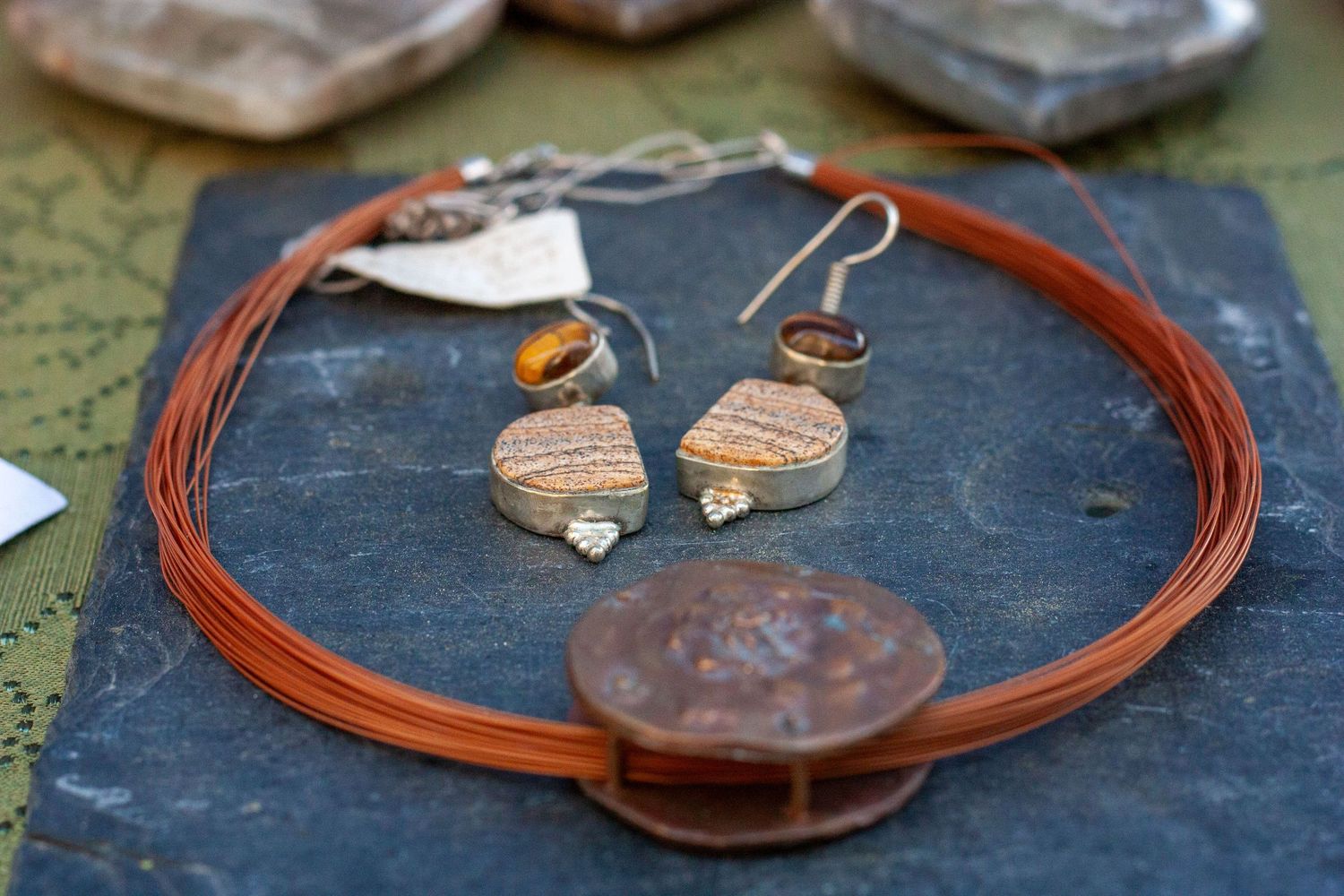 Handmade copper wire necklace with stone pendant displayed alongside matching earrings and rings on a slate surface.