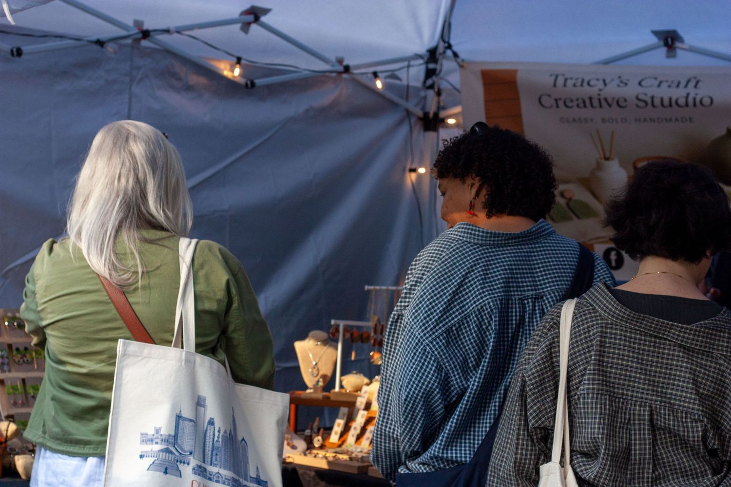 Shoppers browse handmade goods at Tracy's Craft Creative Studio booth at an outdoor market.