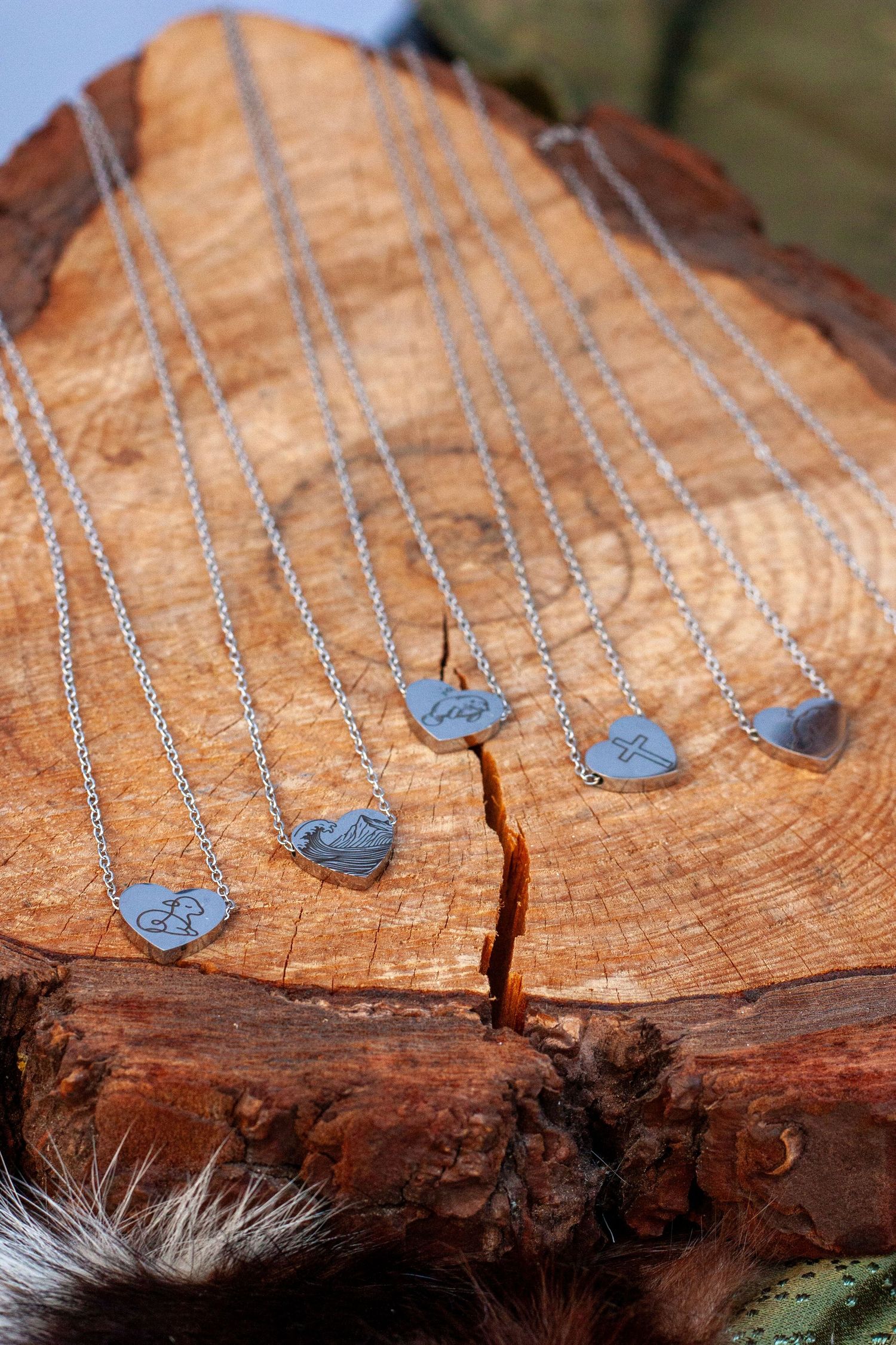 Silver heart pendant necklaces with engraved initials displayed on a rustic wooden log slice.
