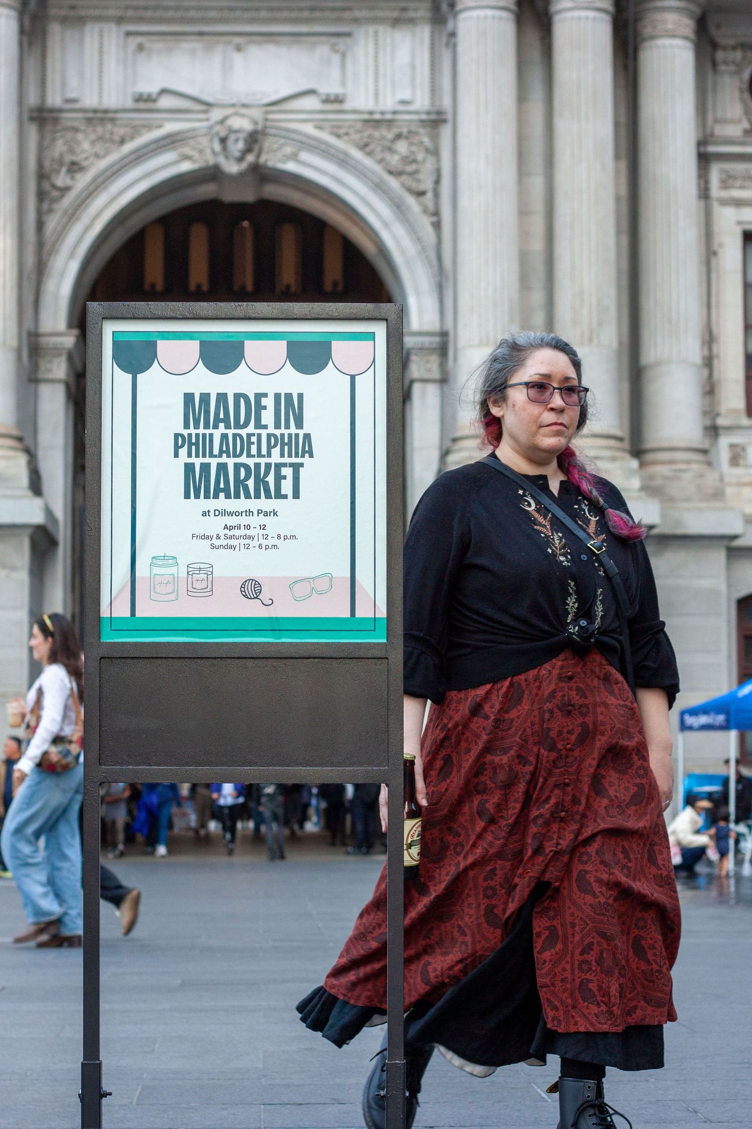 Woman in red skirt stands by Made in Philadelphia Market sign at Dilworth Park entrance.