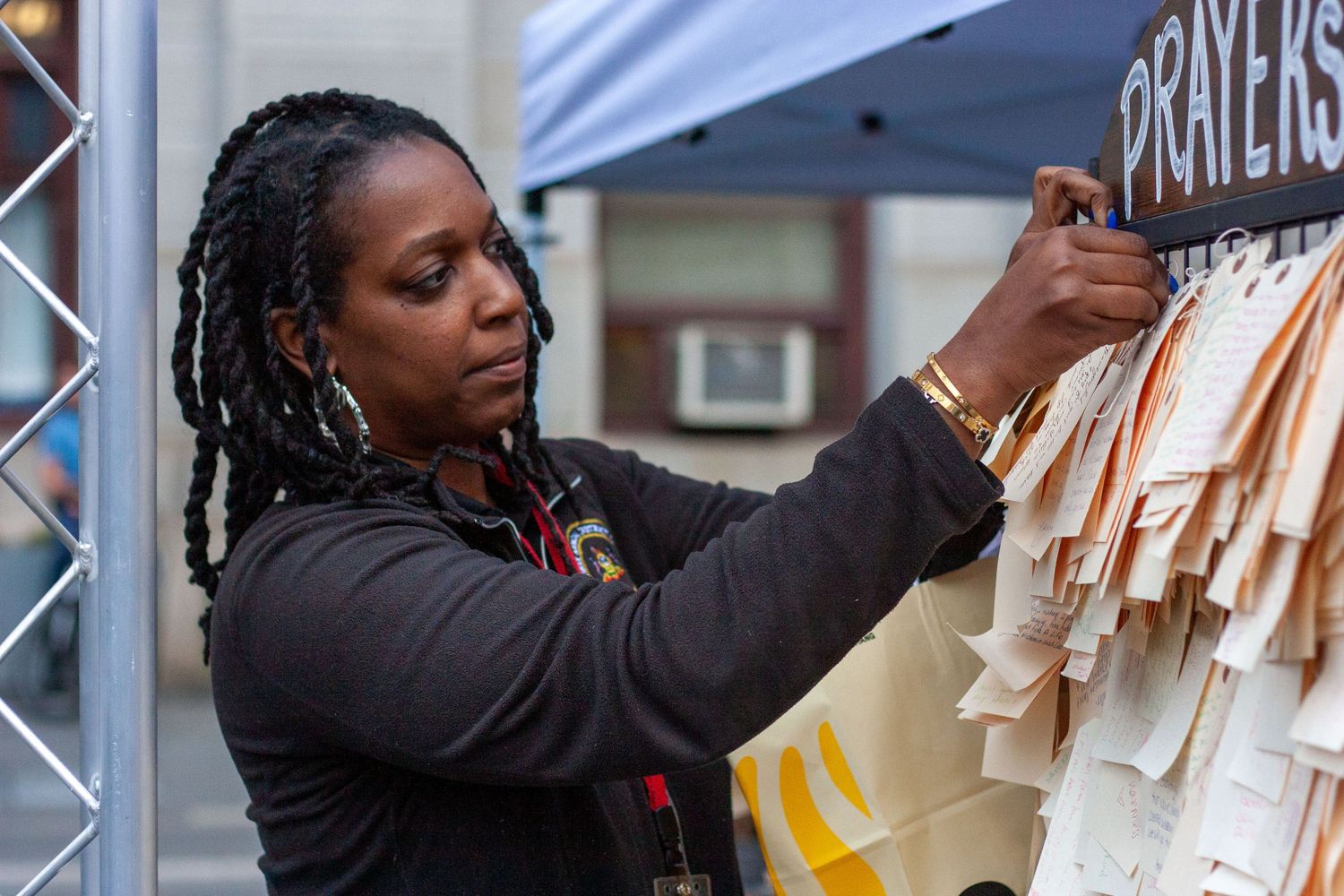 Woman pinning prayer notes to a board at an outdoor community prayers memorial event.