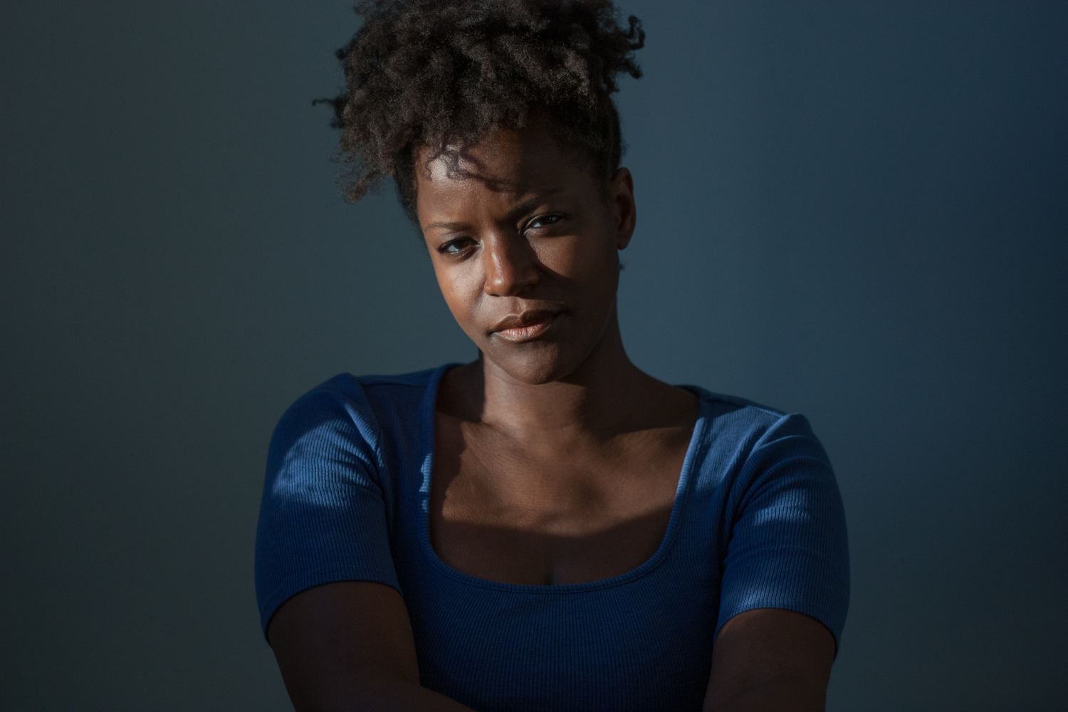 Woman in blue top shown in dramatic lighting against dark background.