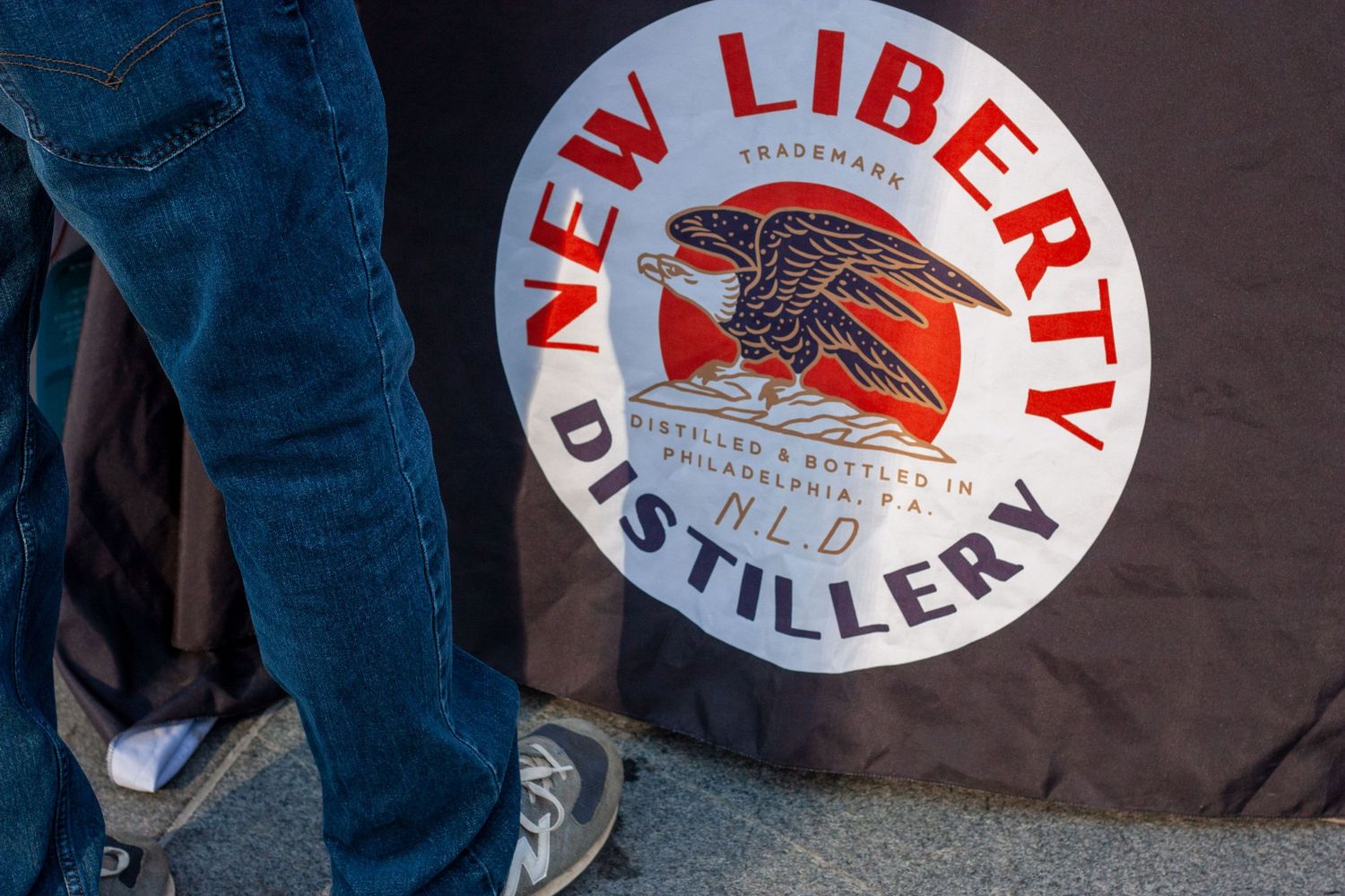 New Liberty Distillery circular logo sign featuring a red eagle, displayed at an outdoor event in Philadelphia, PA.