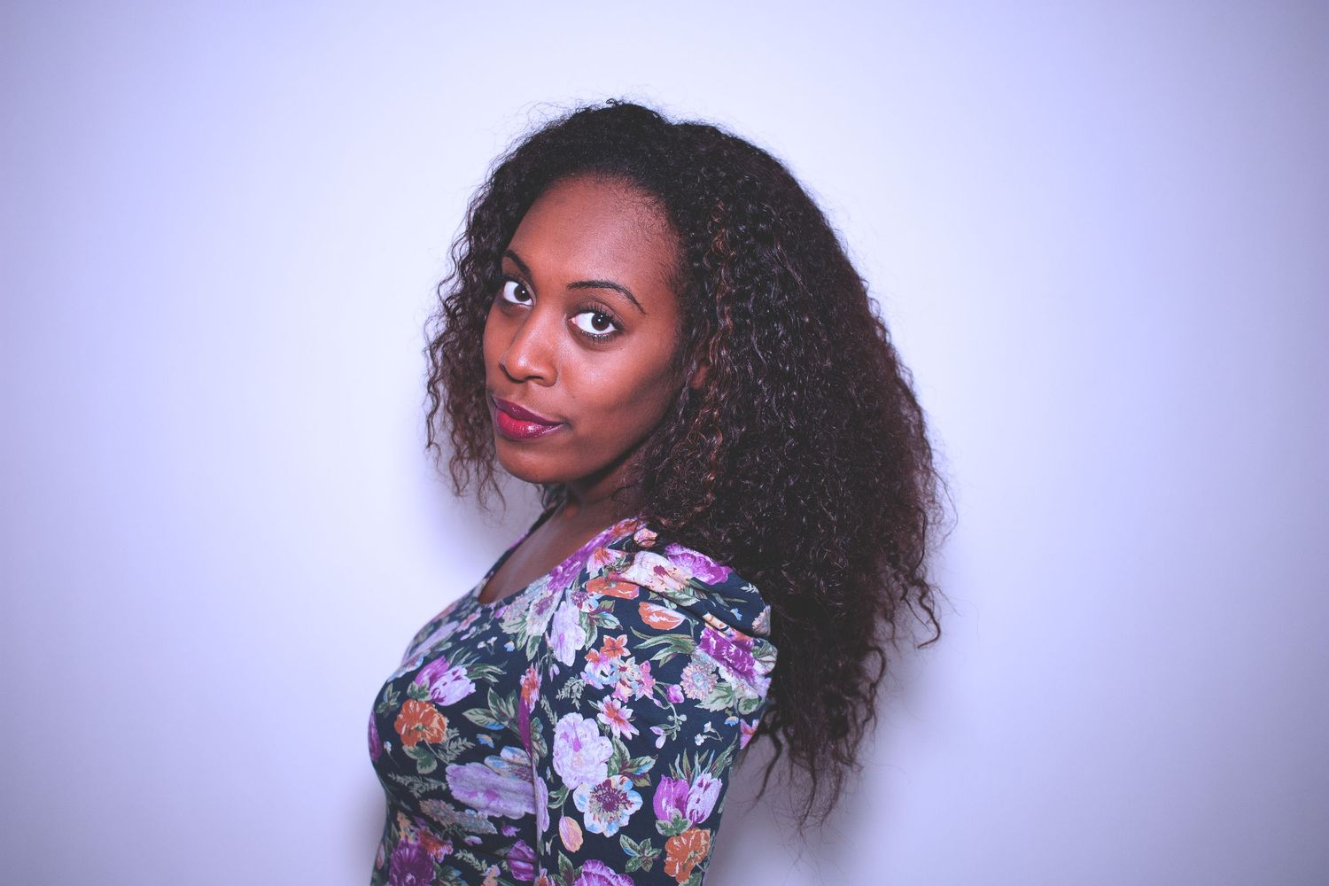 Woman in floral print poses against purple background in artistic portrait series.