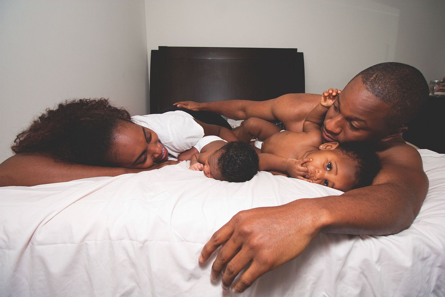 Family resting comfortably on white sheets in natural light.