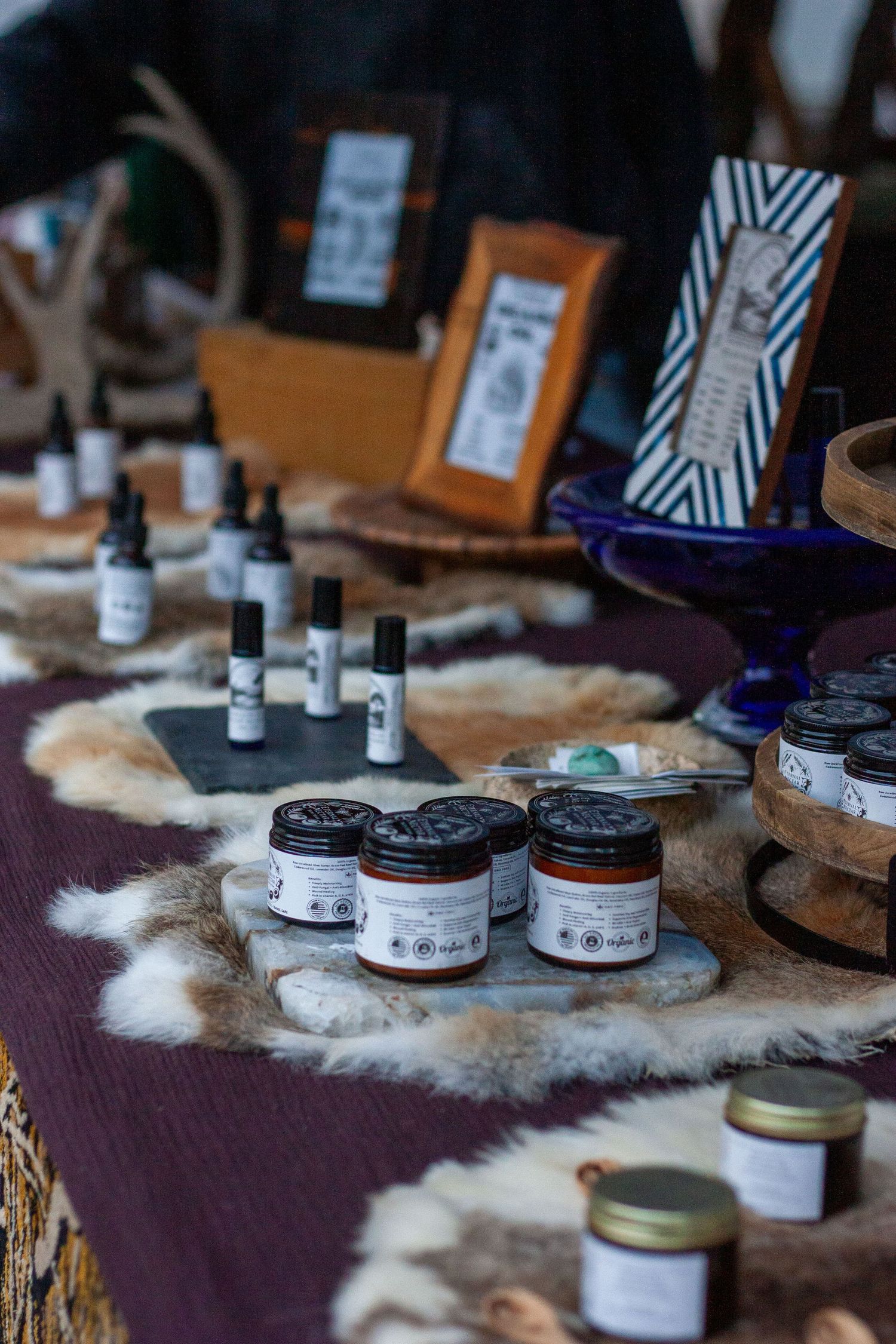 Artisan market stall displaying handcrafted jars, serums, and natural beauty products arranged on fur pelts.