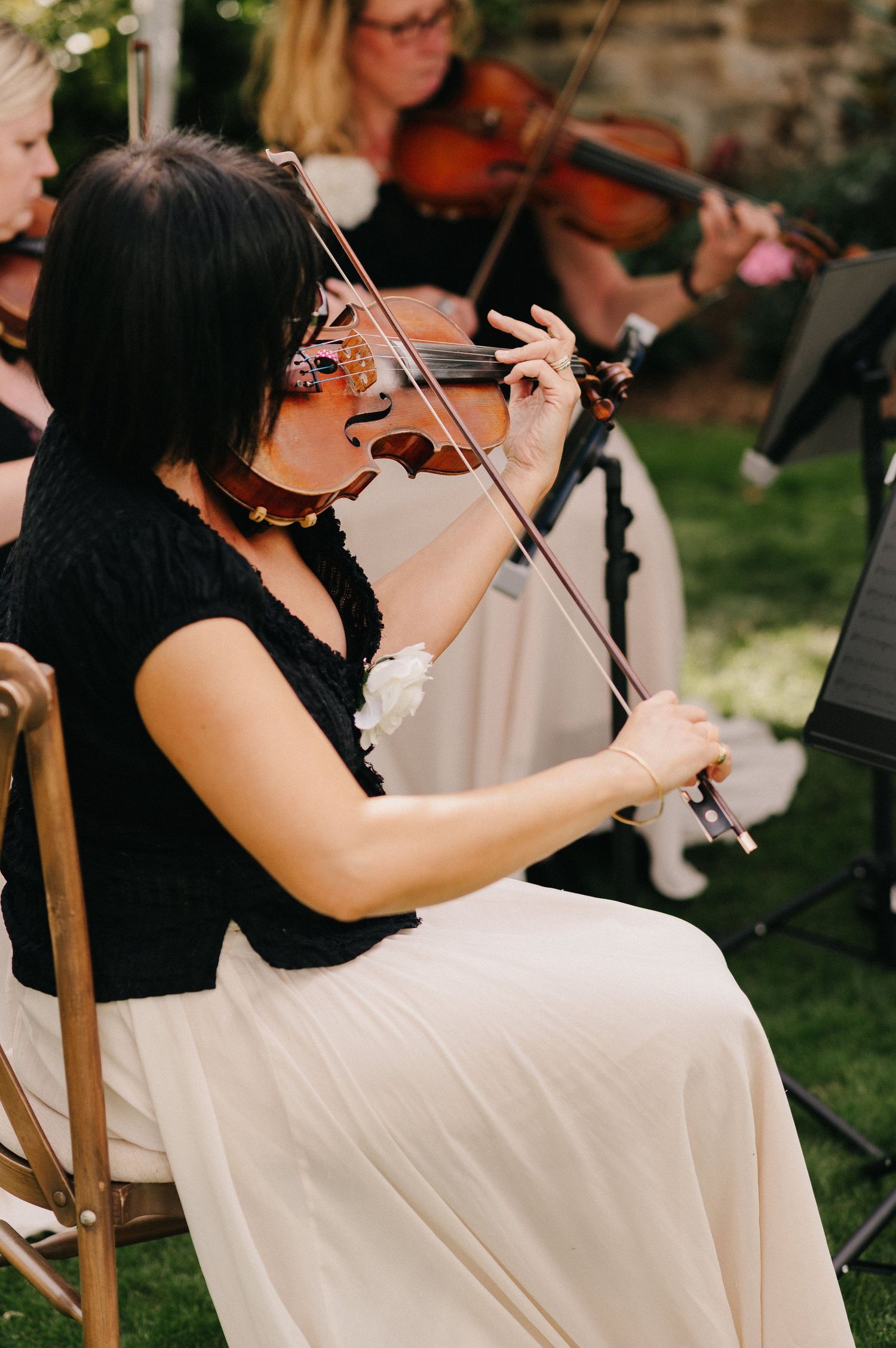 A violinist in a black top and white skirt plays during an outdoor wedding ceremony.