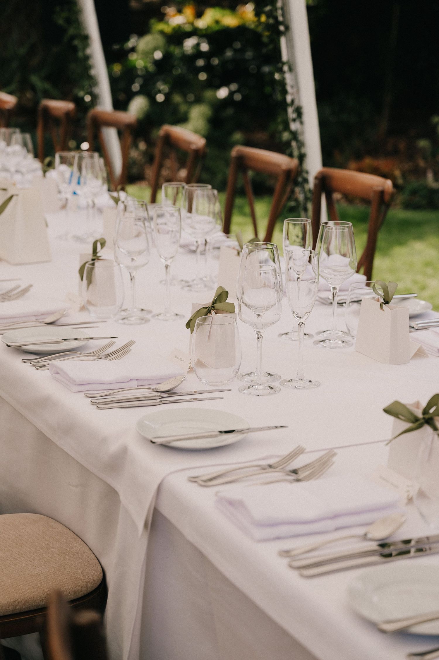 Elegant outdoor wedding reception table set with white linens, crystal glassware, and green ribbon napkin accents.